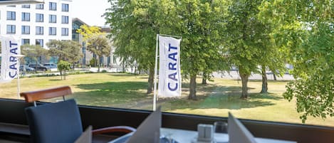 A restaurant with outdoor seating, a view of a grassy area, and flags with the name "CARAT".