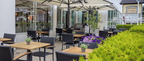 An outdoor seating area with tables and chairs, umbrellas, and potted plants.