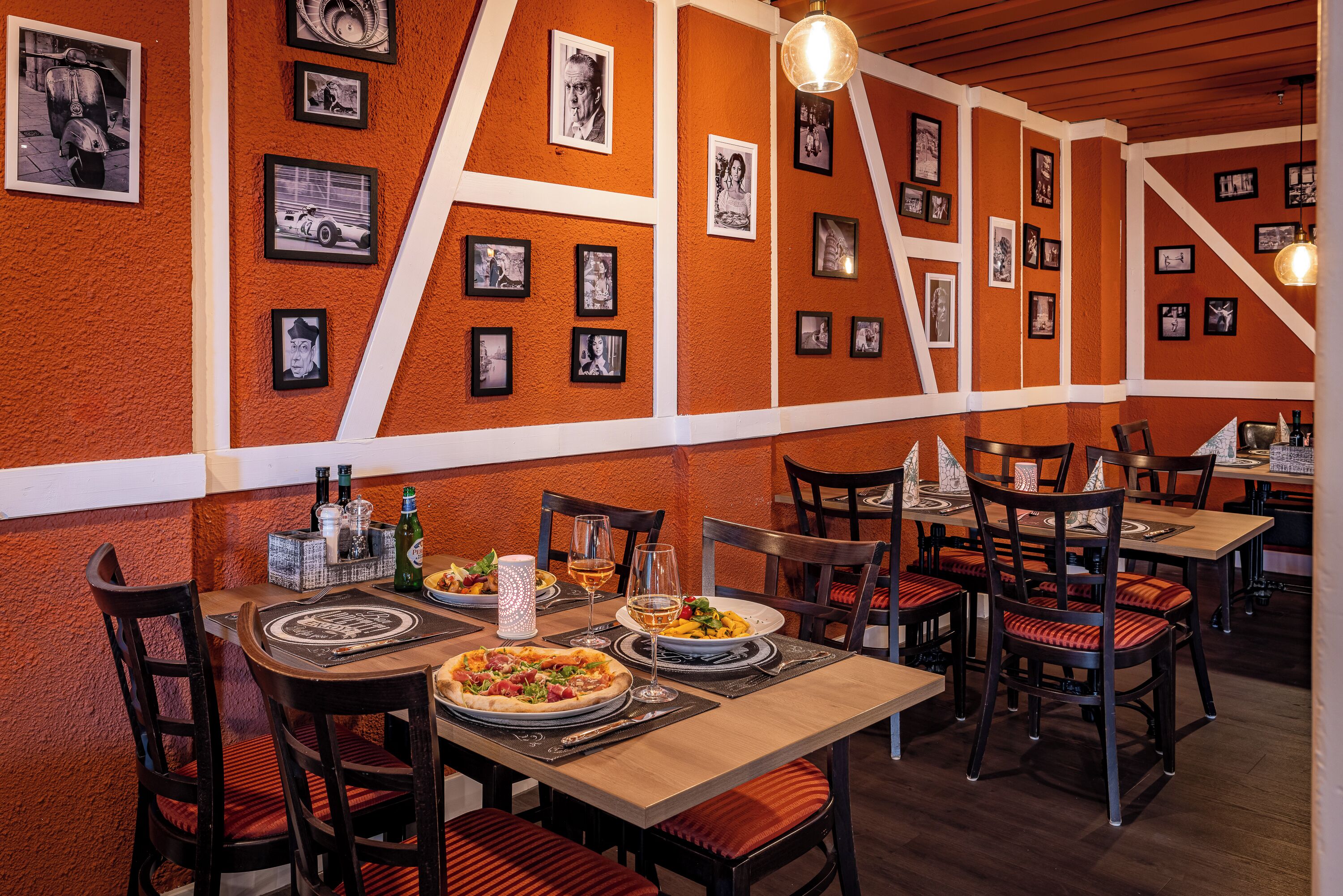 Interior de restaurante con mesas y sillas de madera, y una pared decorada con cuadros enmarcados.