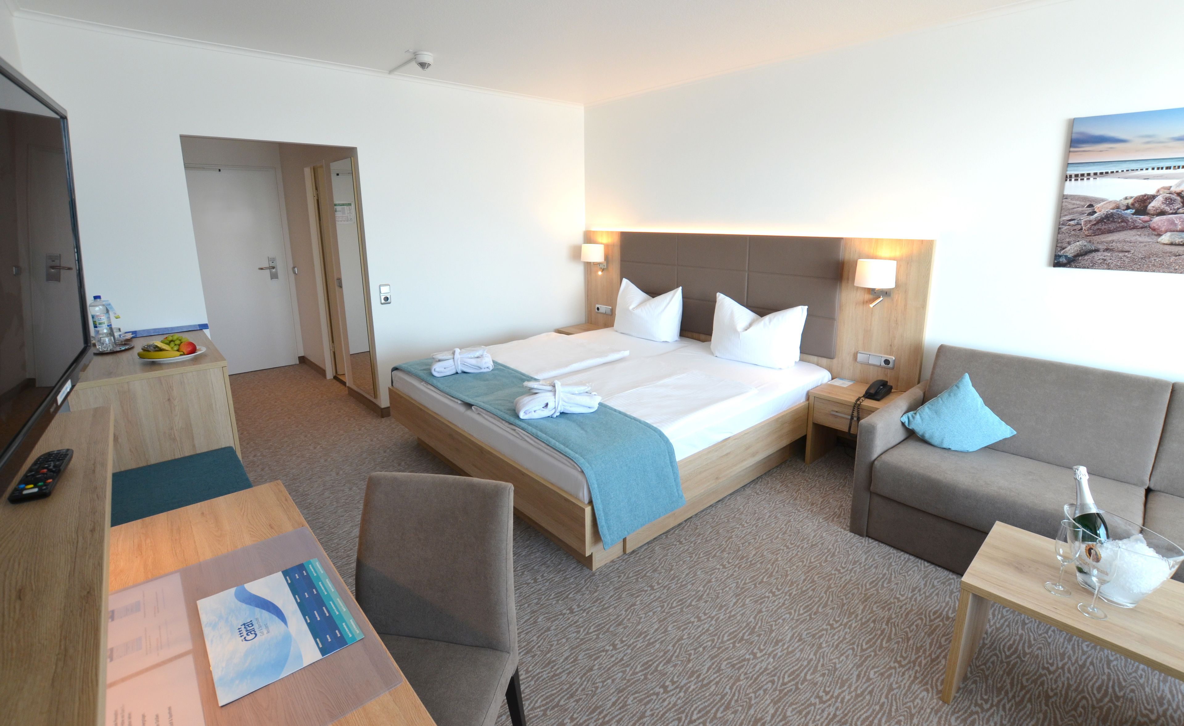 Una habitación de hotel con una cama, un escritorio con una computadora, una silla, un sofá y una mesita con una botella y vasos.