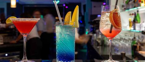 Three cocktails on a bar counter with a blurred background of a bar and people.