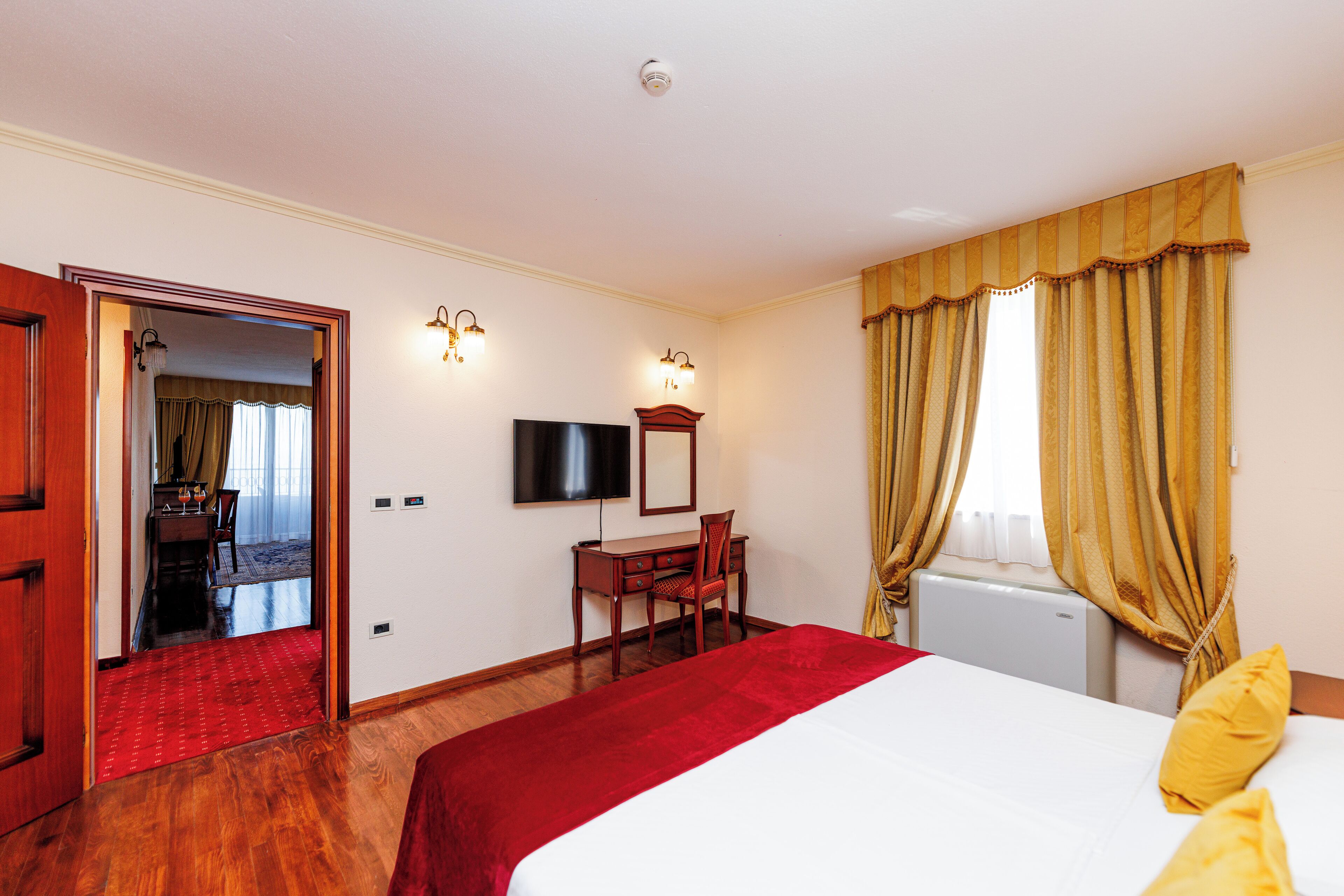A hotel room with a bed, a desk with a chair, a television, and a window with curtains.