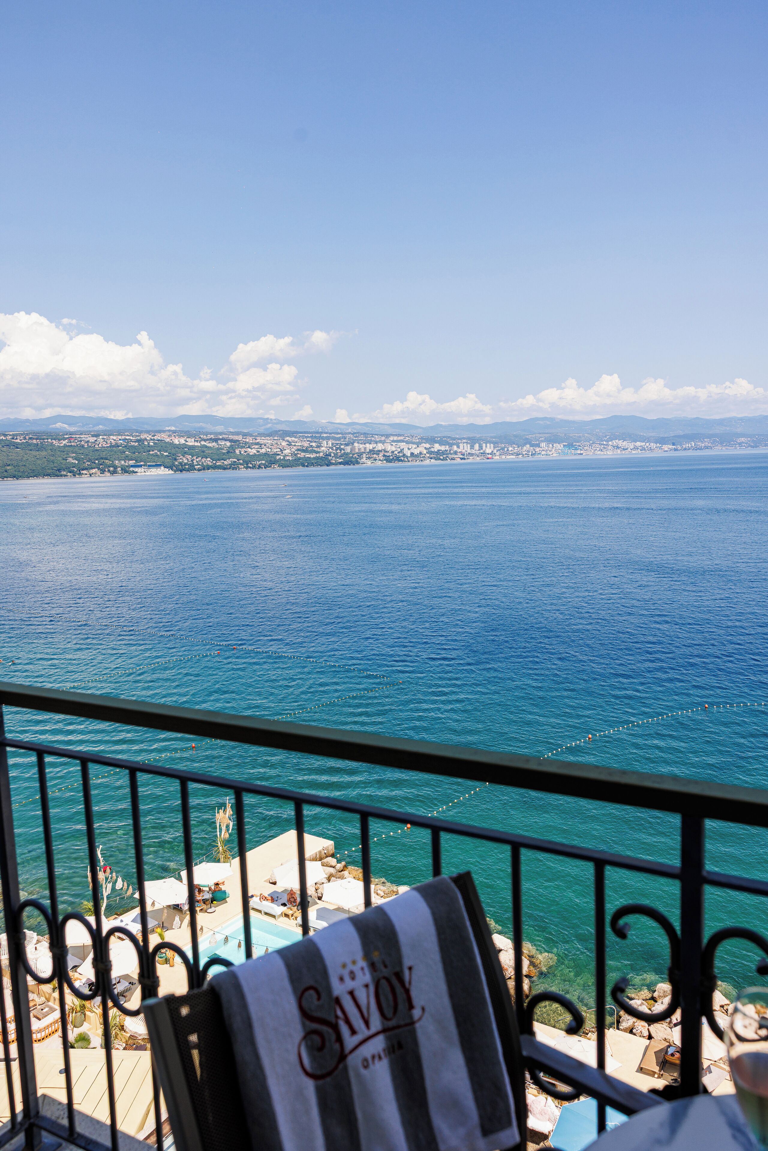 A balcony with a view of the sea and a distant cityscape.