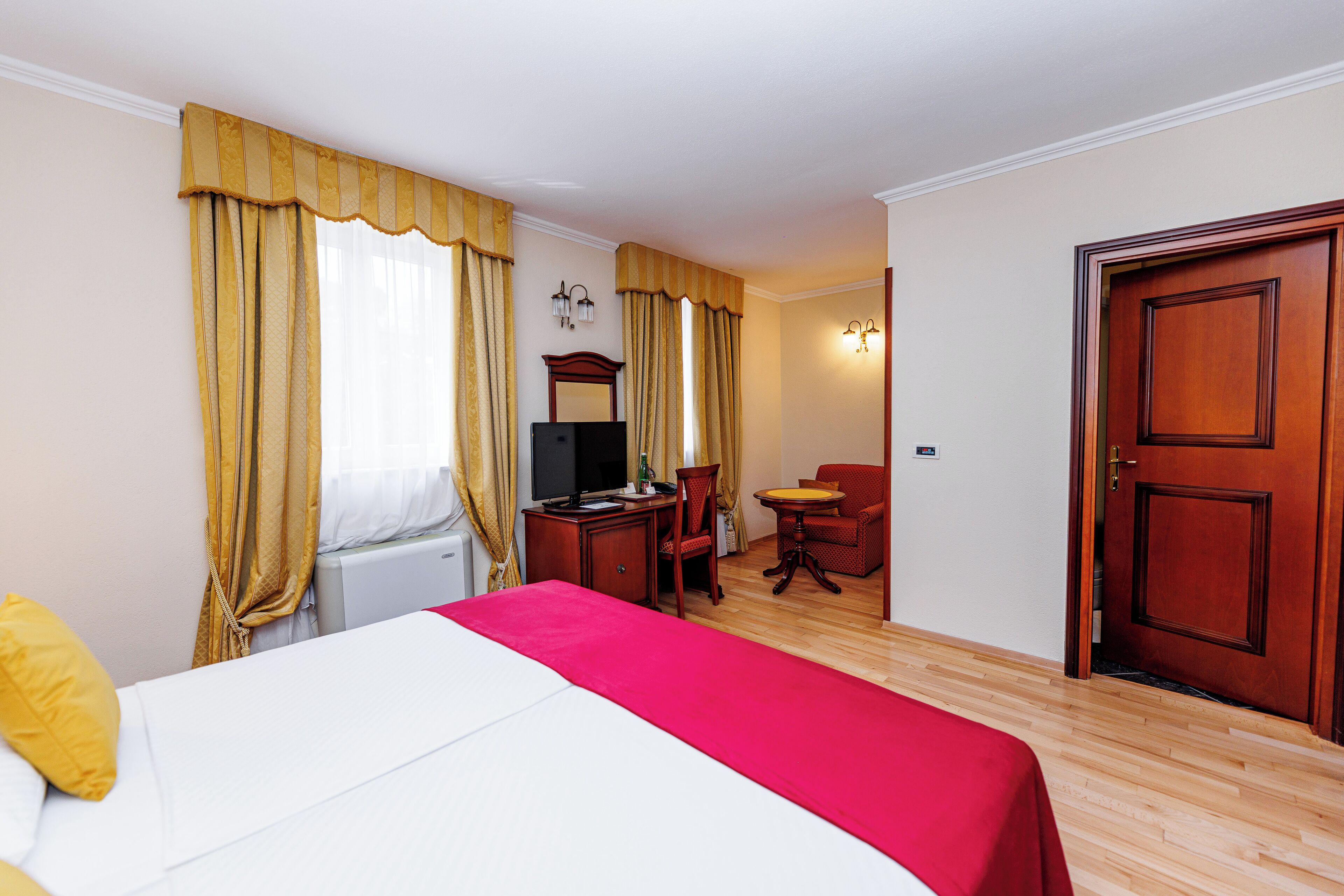 Une chambre d’hôtel comprenant un lit, un bureau avec un ordinateur, une chaise, une petite table et une porte.