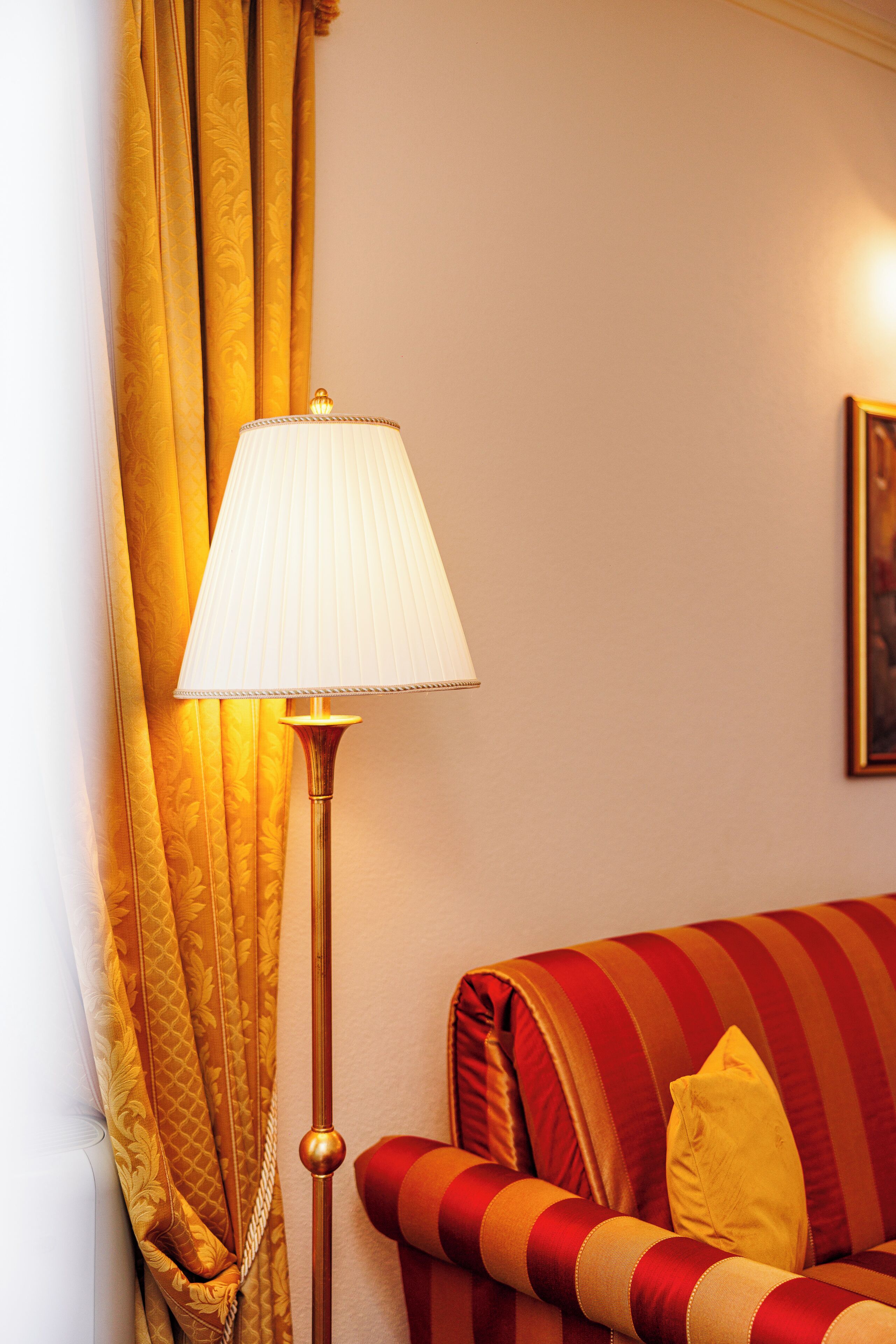 Una habitación con una lámpara de pie, un sofá con cojines a rayas y cortinas.