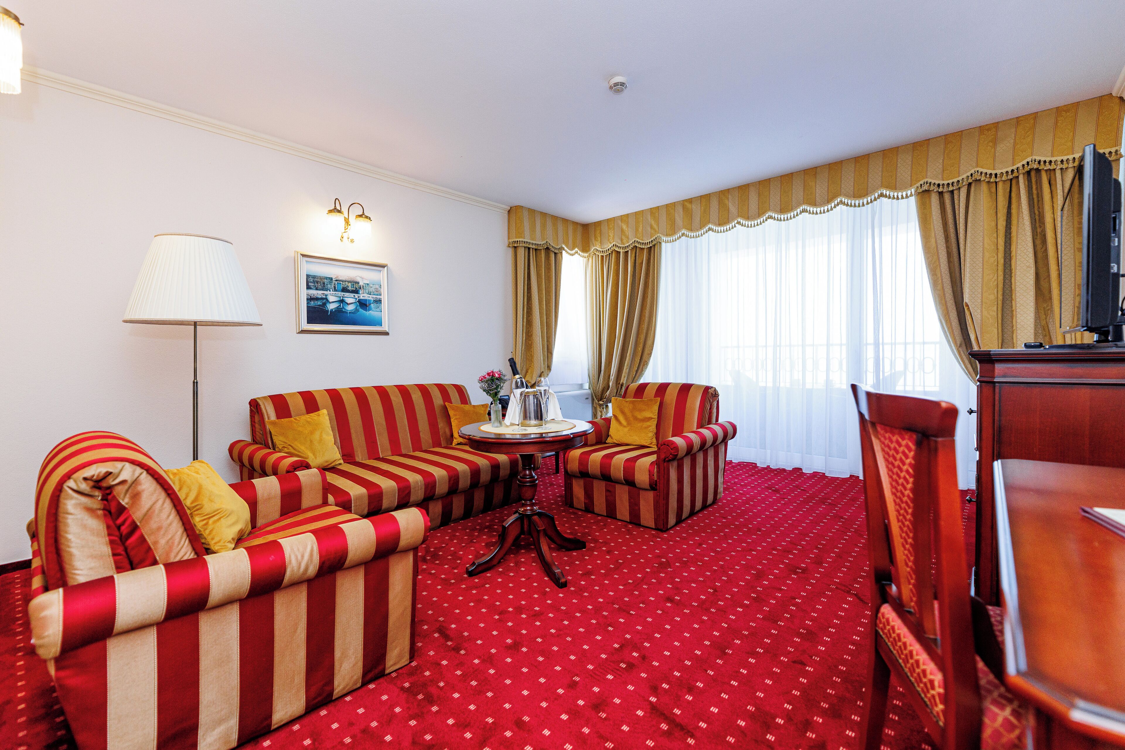 A hotel room with striped sofas, a small round table, a lamp, and a TV.