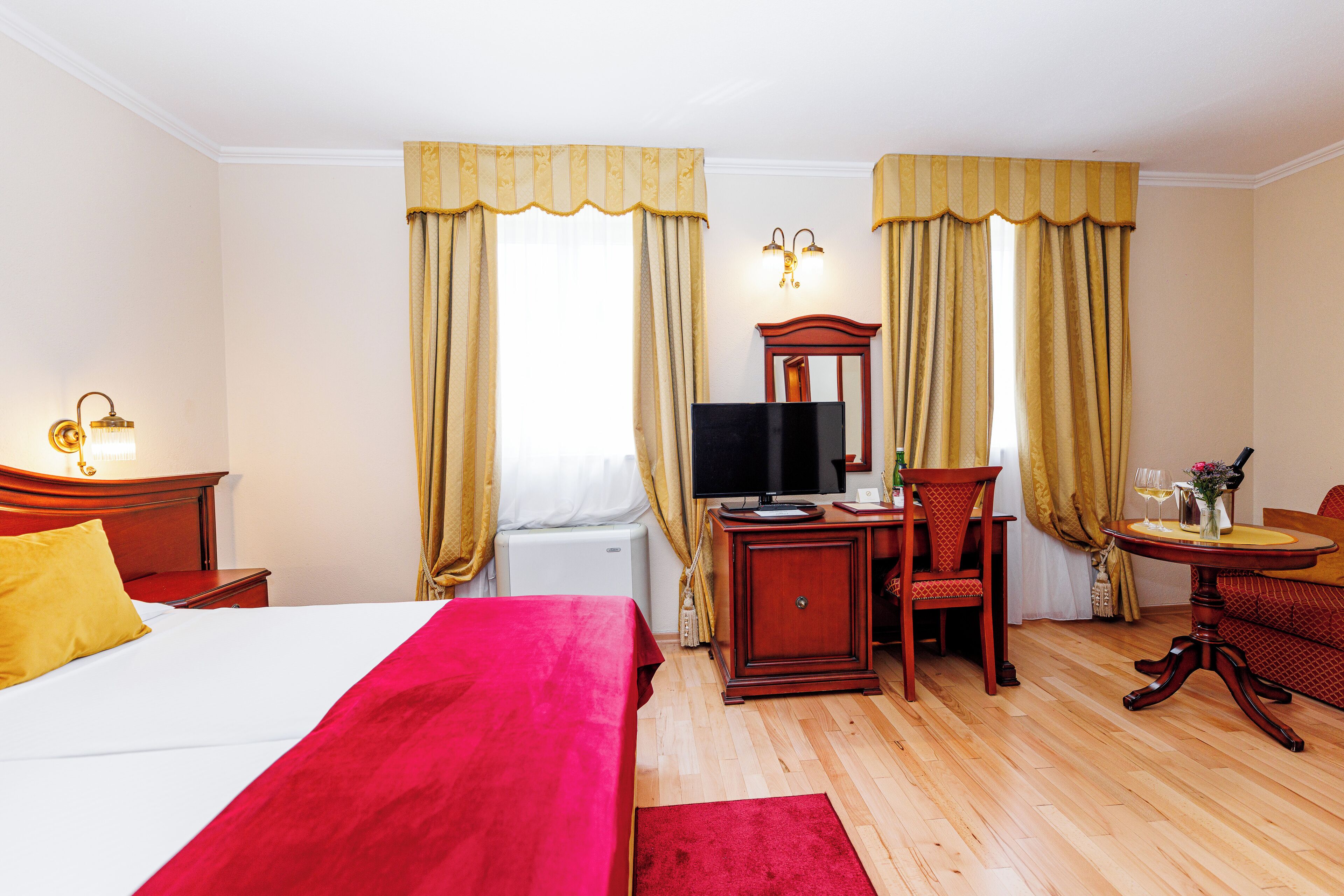 Ein Hotelzimmer mit einem großen Bett, einem Schreibtisch mit Stuhl, einem Fernseher und einem Esstisch mit Stuhl.