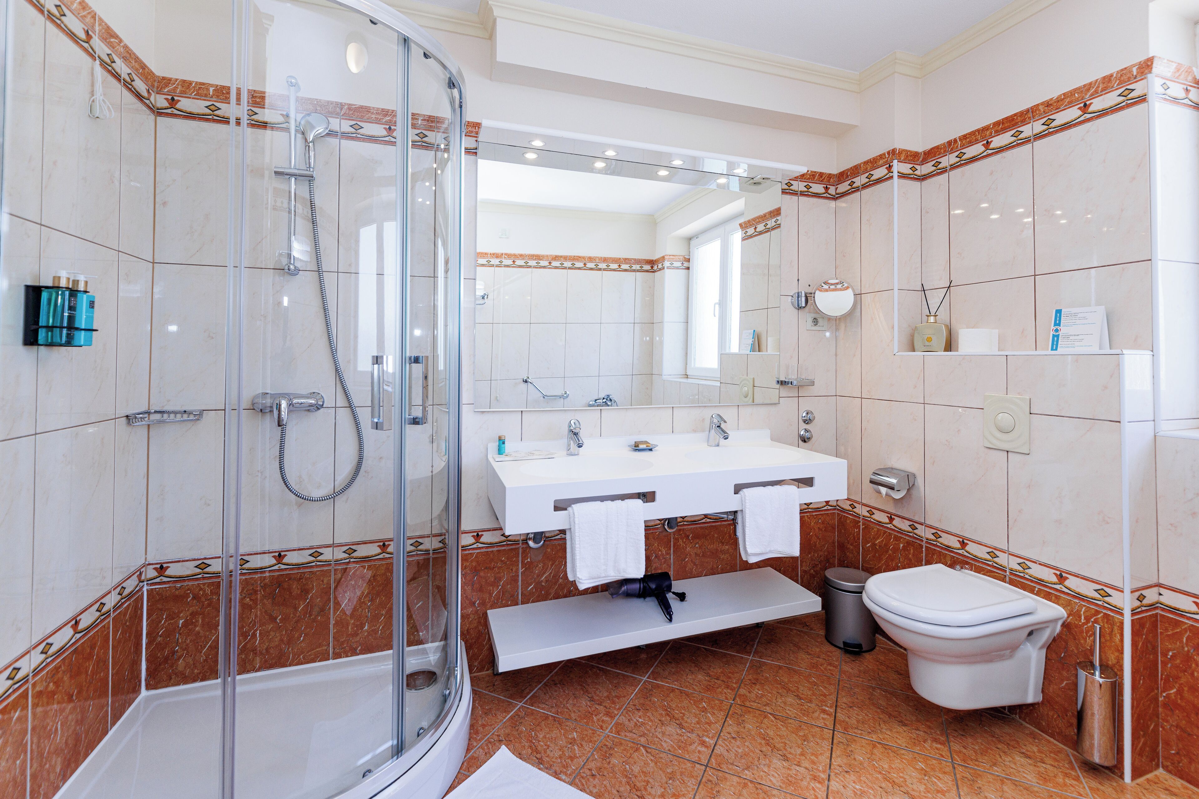 Un baño moderno con ducha acristalada, lavamanos blanco con dos espejos y un inodoro.