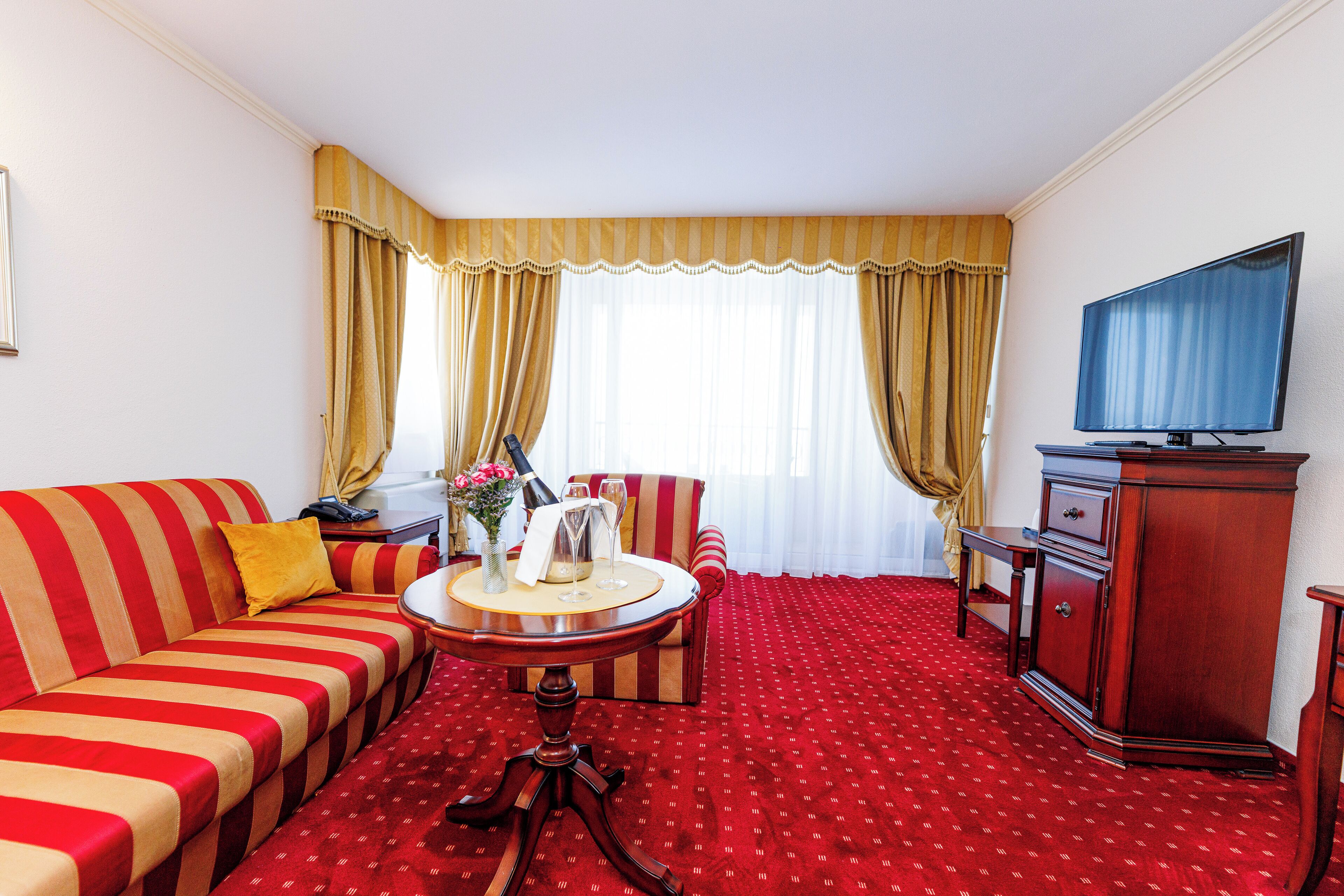 A hotel room with a red carpet, striped sofa, and a television on a wooden cabinet.
