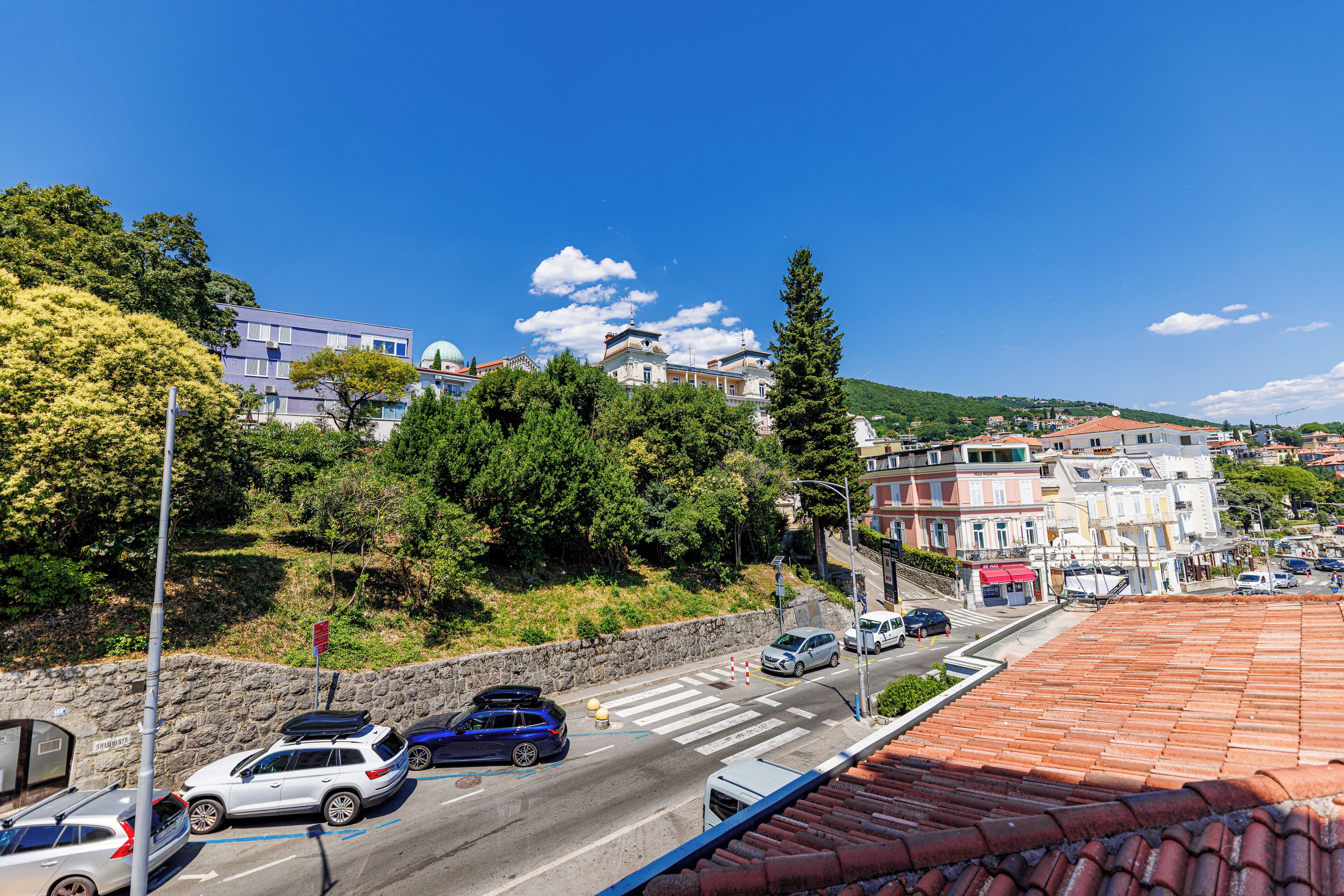 Une vue de rue avec des voitures garées le long du bord, des bâtiments en arrière-plan et un ciel bleu dégagé.