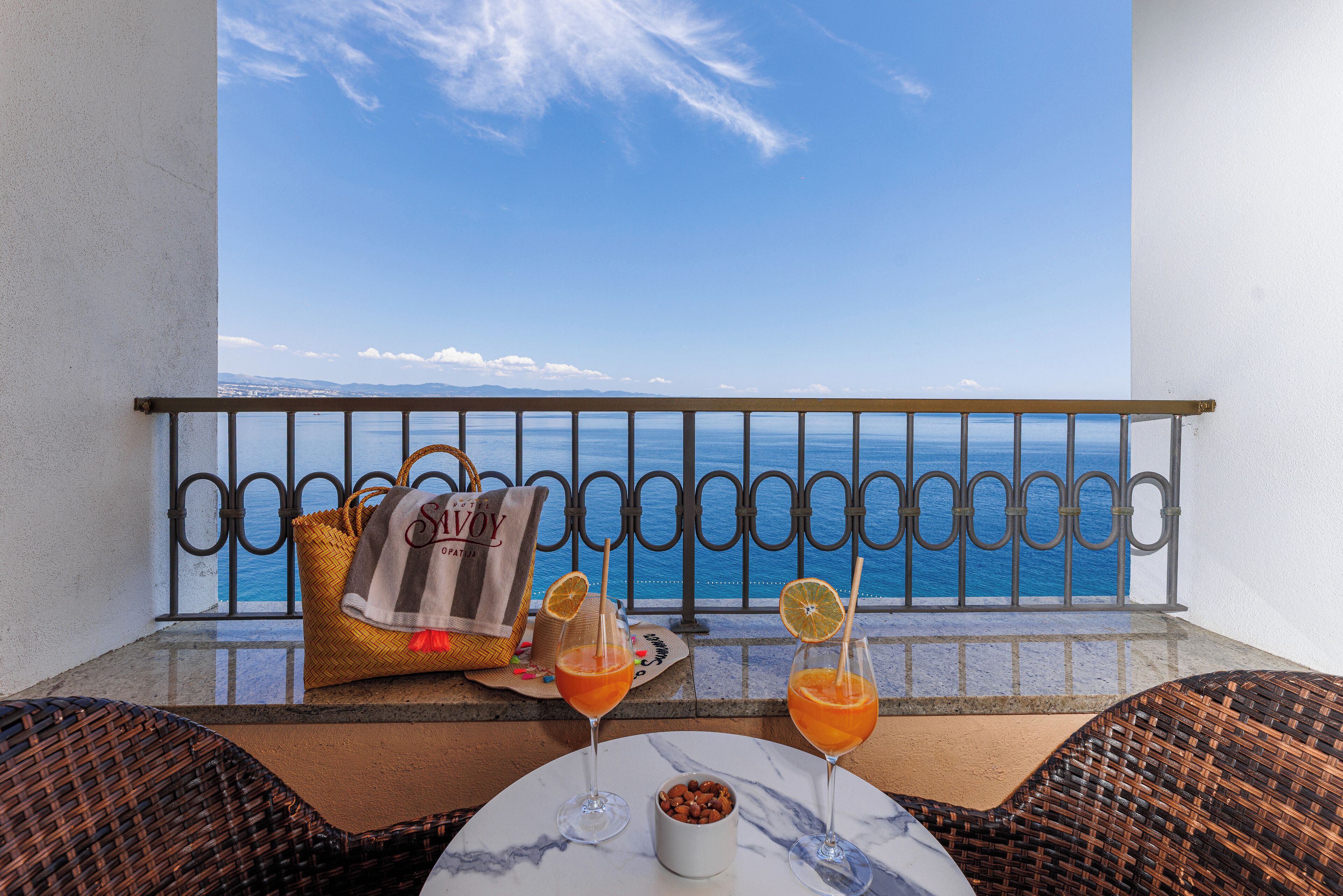 A balcony with a view of the sea, wicker furniture, a table with drinks, and a towel.