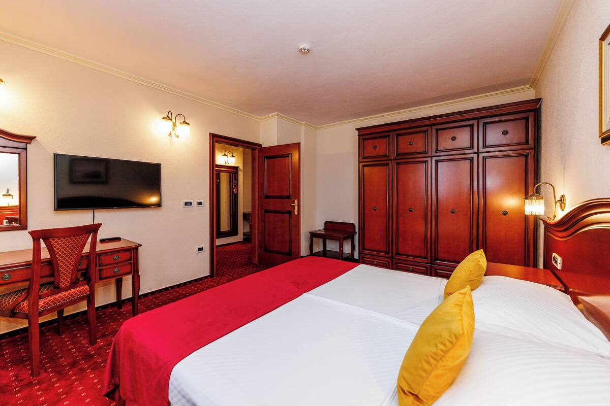 A hotel room with a bed, a desk, a chair, a television, and a wardrobe.