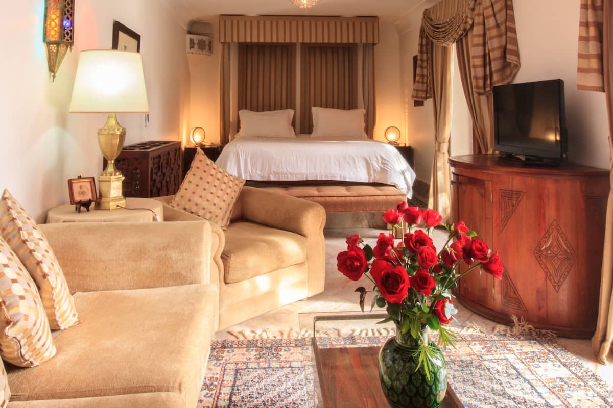 A hotel room with a bed, sofa, TV, and a vase of red roses.