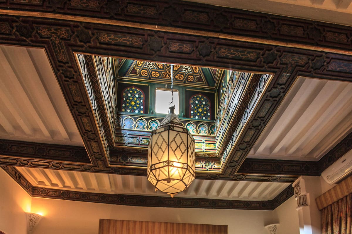 A traditional room with a large bed, two bedside tables, a chair, and ornate ceiling details.