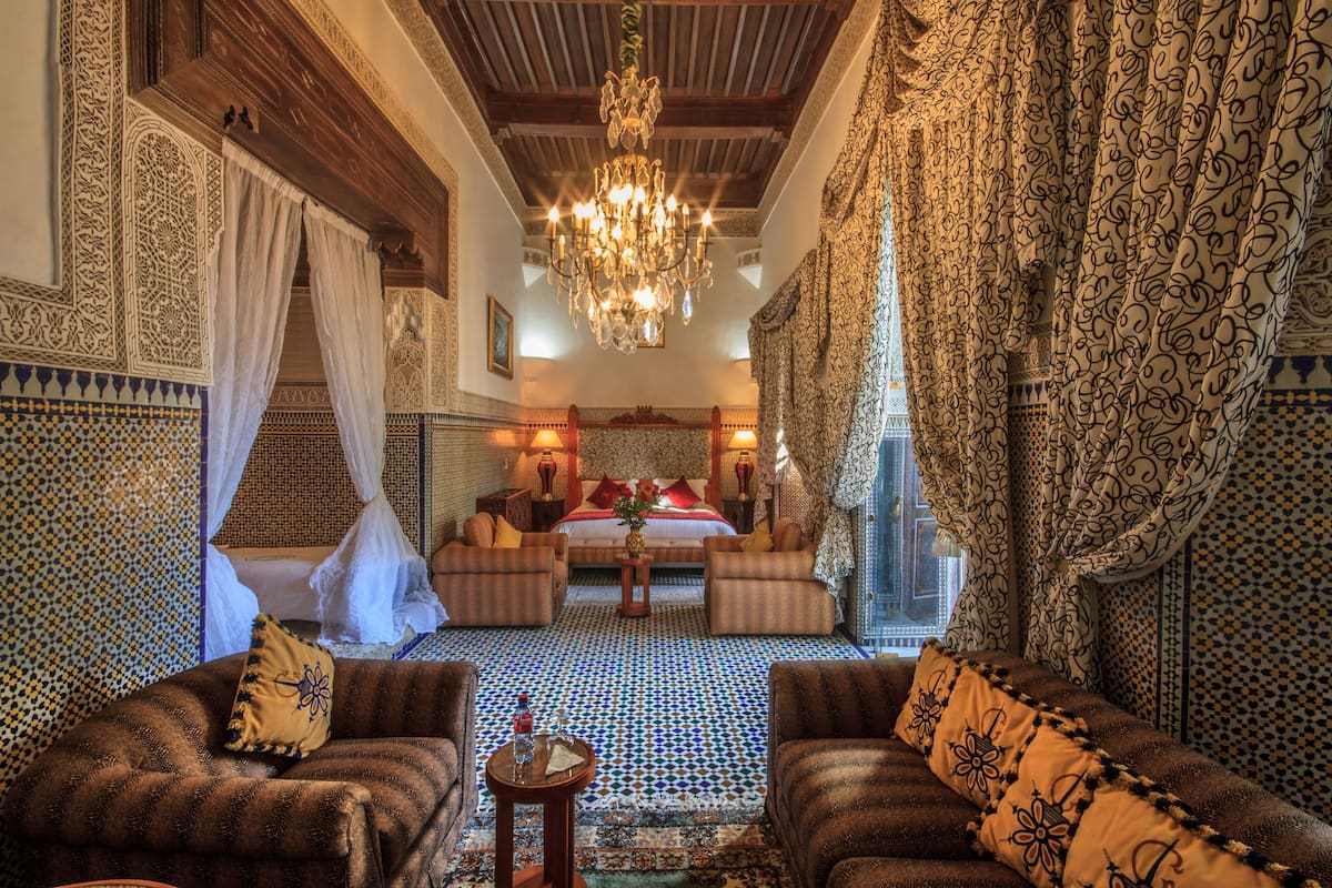 A traditional Moroccan room with a patterned floor, a chandelier, and a bed with a canopy.