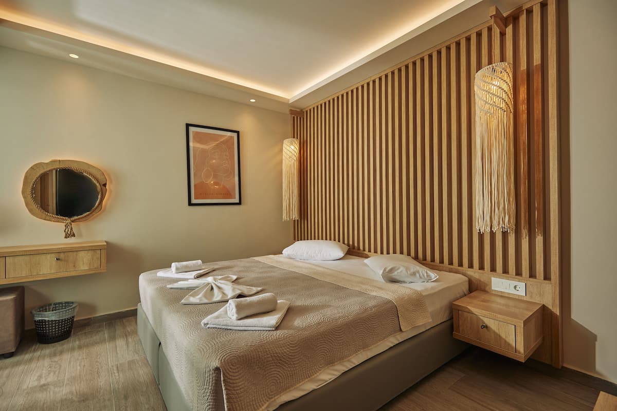 A modern hotel room with a large bed, wooden panel wall, a round mirror, and a bedside table with a lamp.