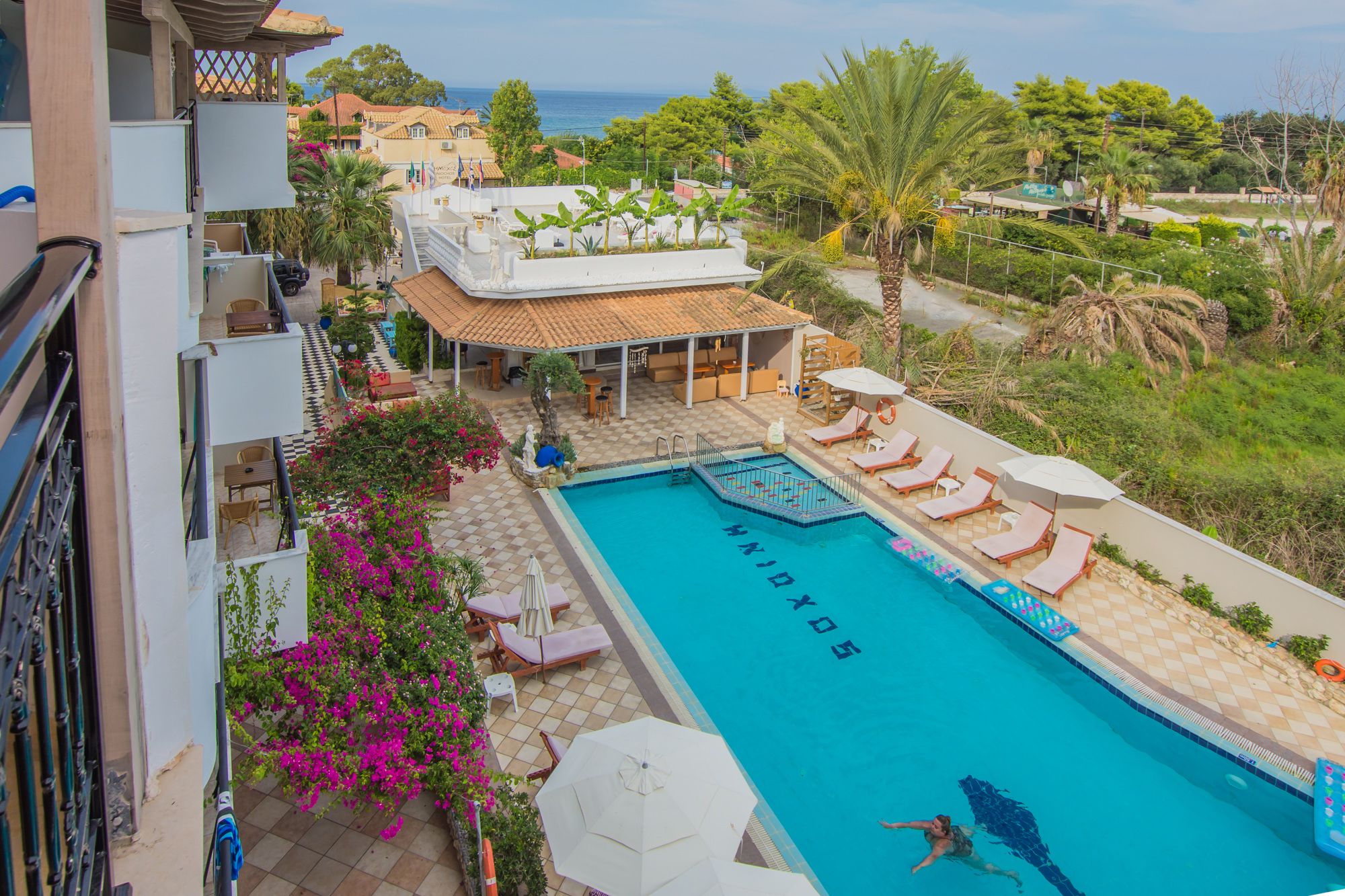 Una piscina en la azotea con vista al mar, rodeada de palmeras y una zona de estar cubierta.