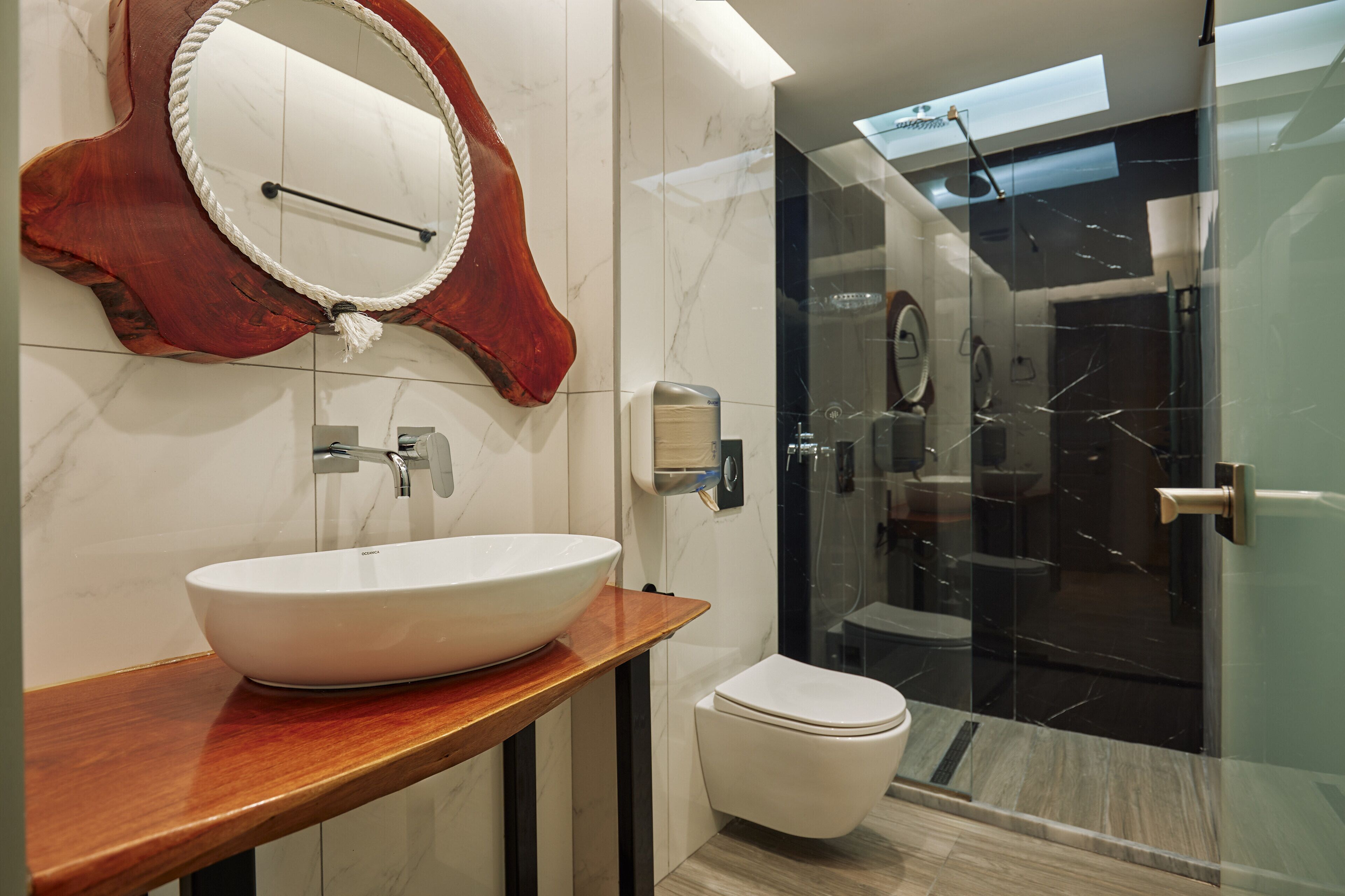 A modern bathroom with a large oval sink, a wooden countertop, a white toilet, and a glass shower enclosure.