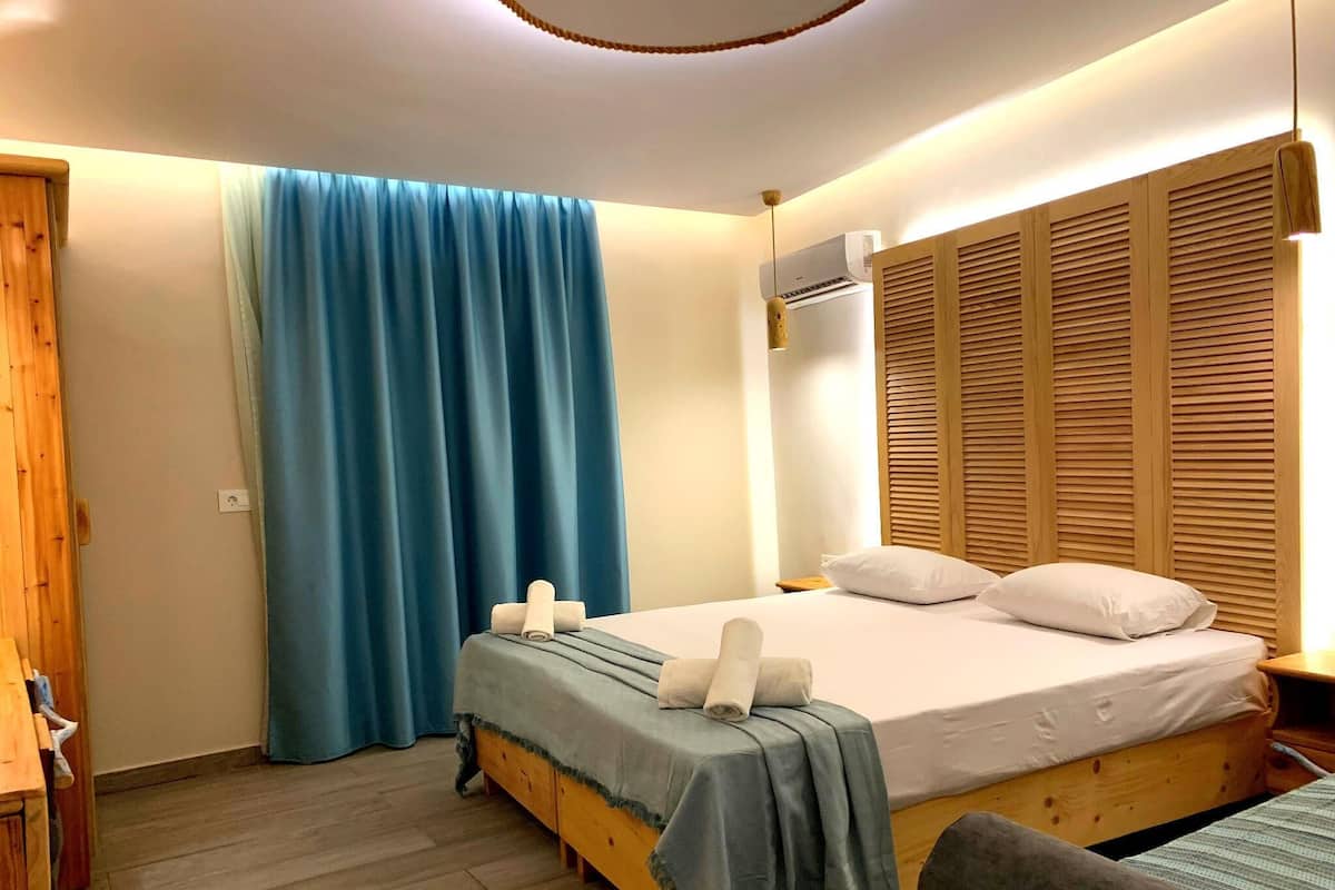 A bedroom with a bed, a wooden wardrobe, a blue curtain, and an air conditioning unit.