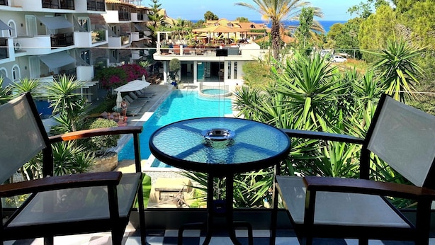 A poolside view with a table and chairs, a pool, and a view of the resort buildings and ocean.