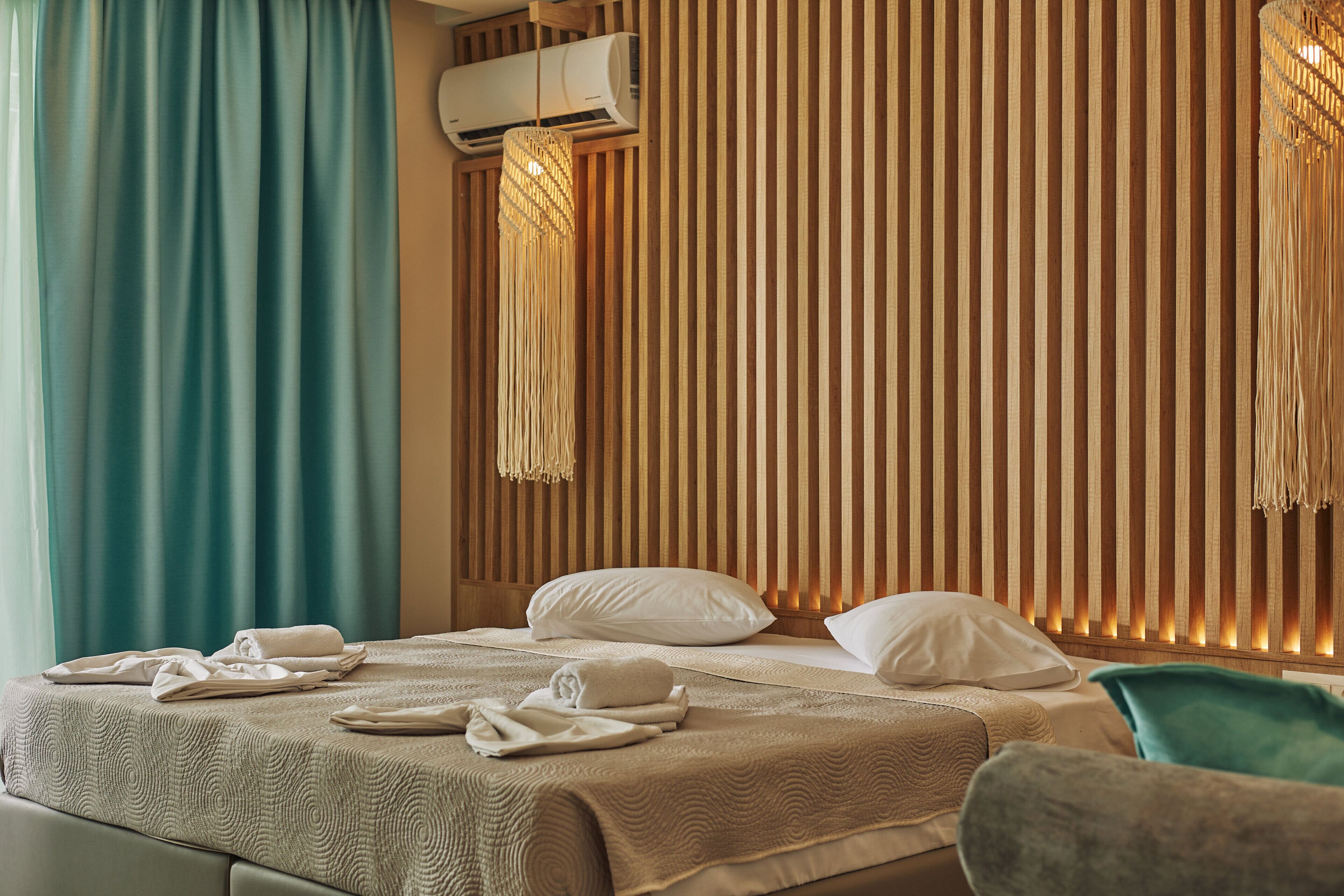 A hotel room with a bed, pillows, towels, an air conditioner, and a wooden slat wall.