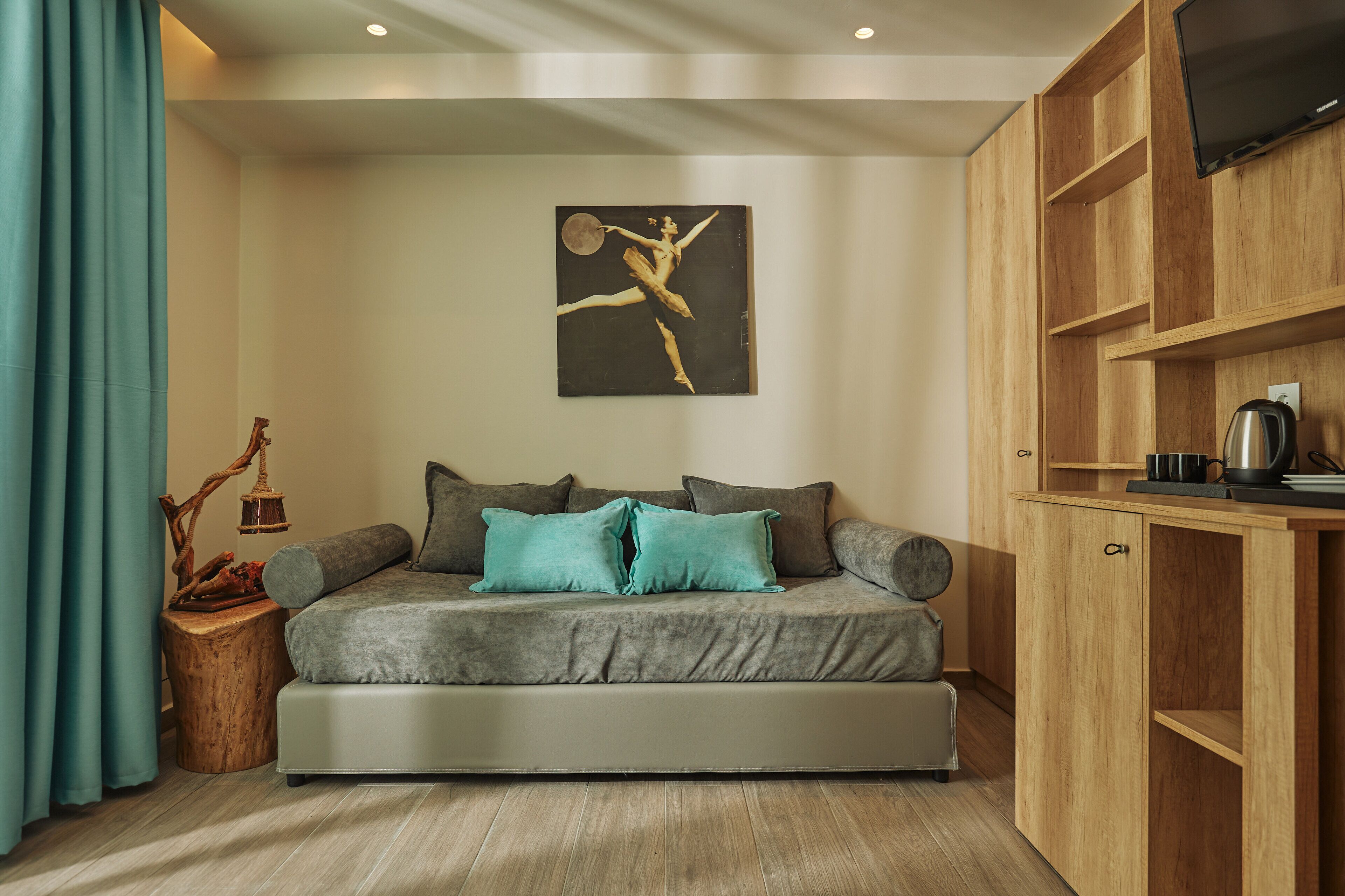 A modern living room with a sofa, teal cushions, a wooden side table, a wall-mounted TV, and a wooden cabinet.