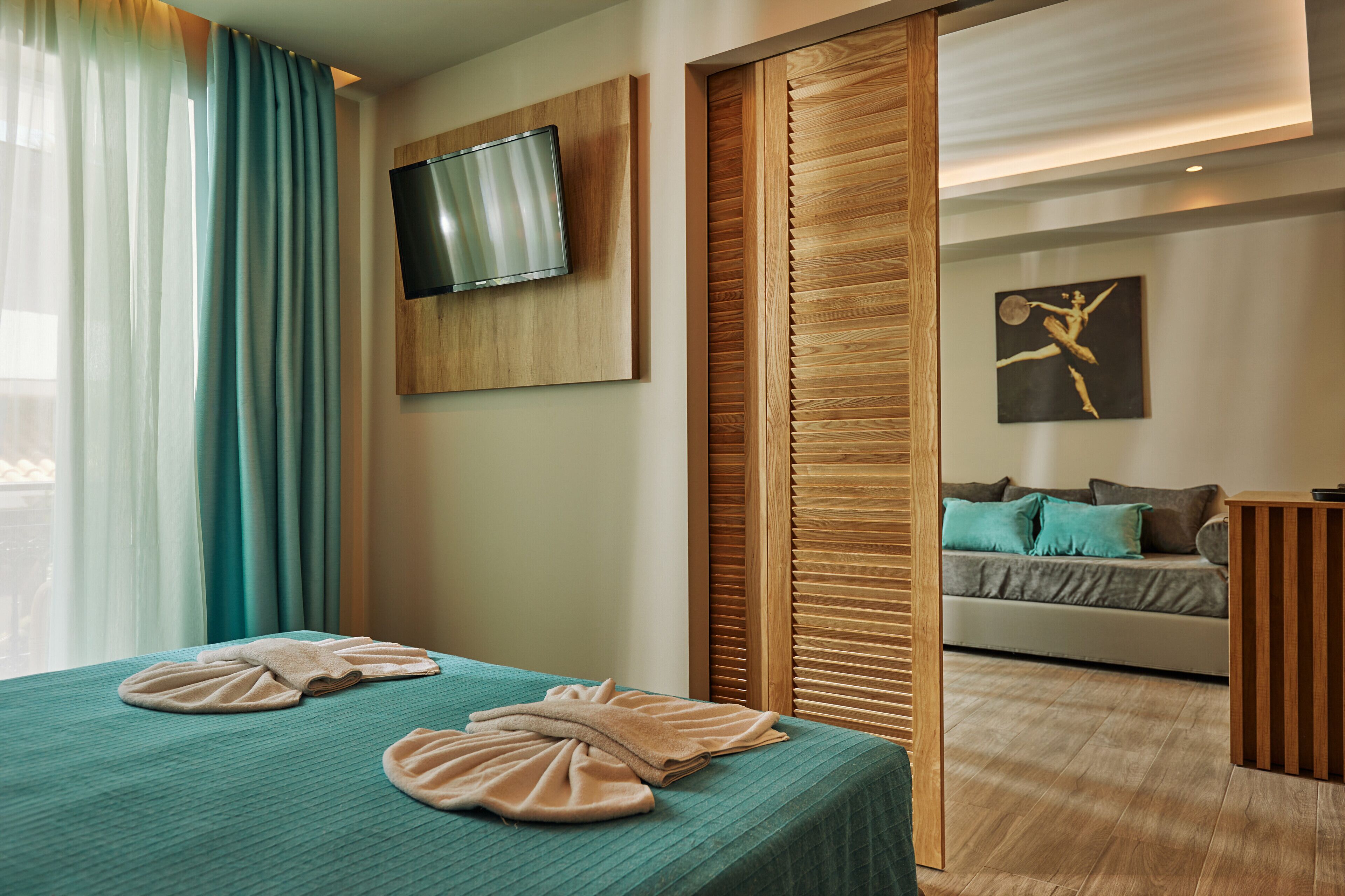 A hotel room with a bed, a TV mounted on the wall, a wooden partition, and a painting on the wall.