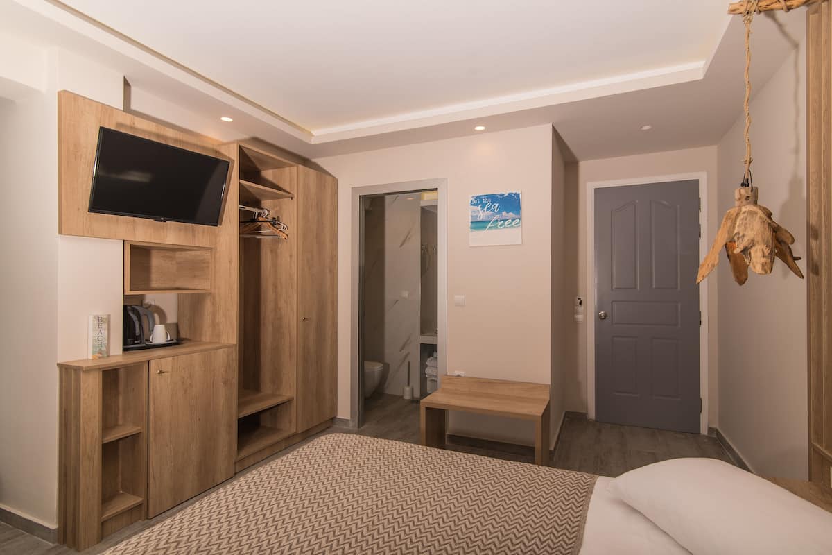 A bedroom with a bed, a wooden wardrobe, a TV mounted on the wall, a small table, and a door leading to another room.