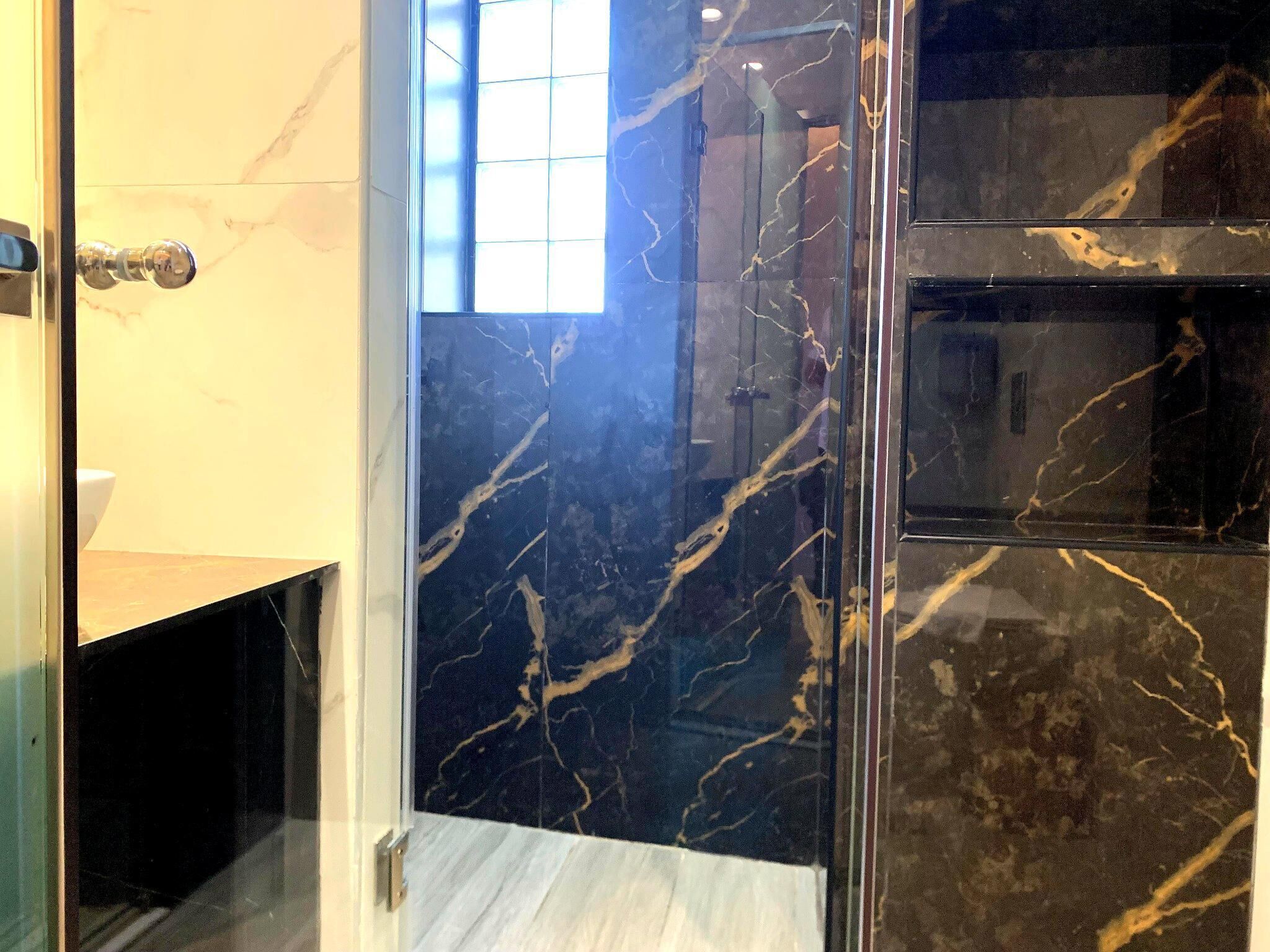 A bathroom with a glass shower enclosure, marble walls, and a white sink.