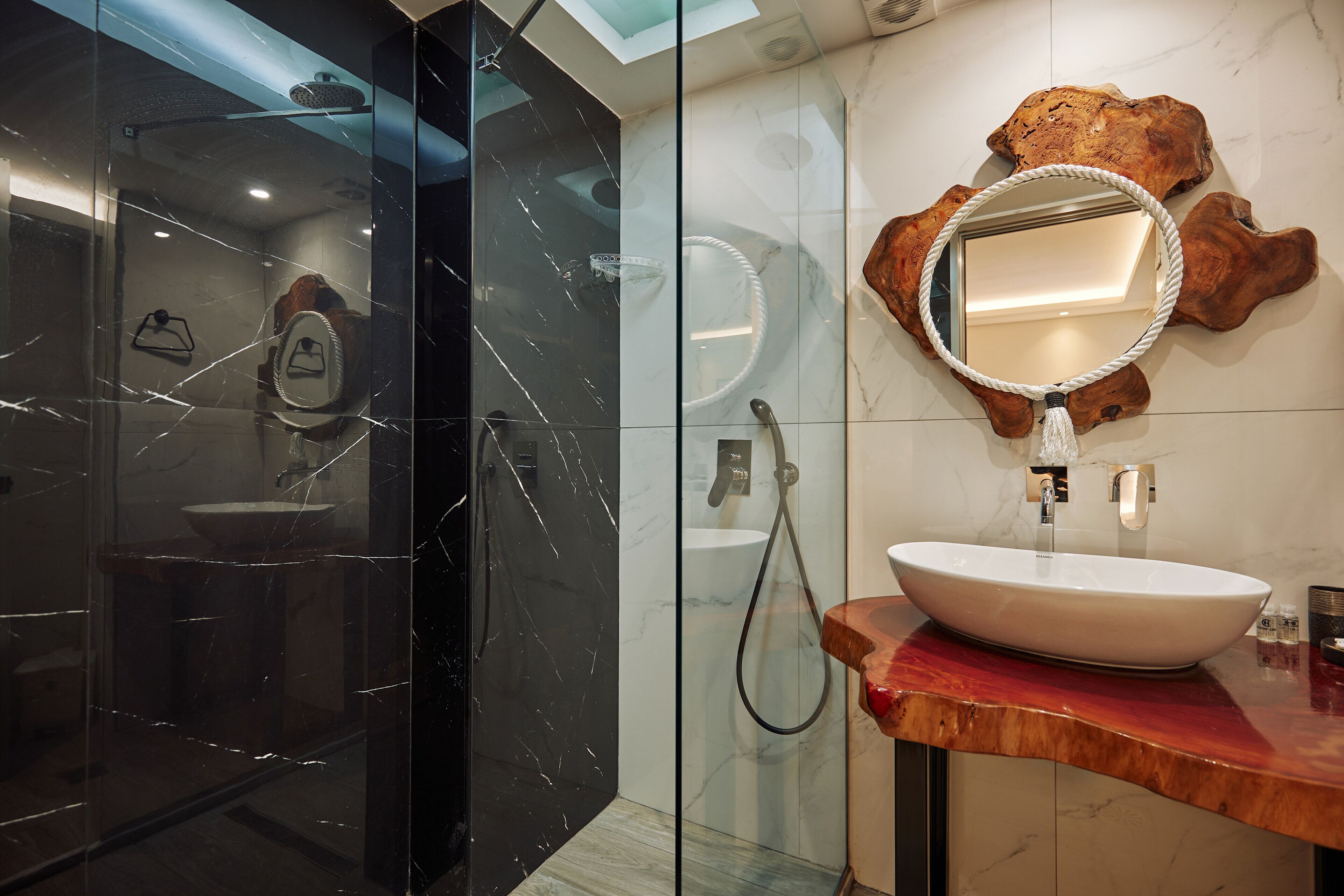 Een moderne badkamer met een douche met glazen wand, een houten wastafelmeubel met een grote spiegel en een wand betegeld met marmer.
