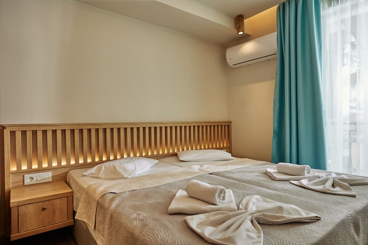 A hotel room with a wooden headboard, two beds, a nightstand, and a window with curtains.