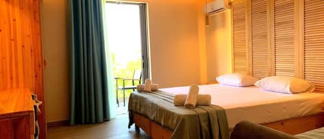 Una camera d'albergo con pavimento in legno, un letto con copripiumino verde, un armadio in legno, una finestra con tende e un climatizzatore.