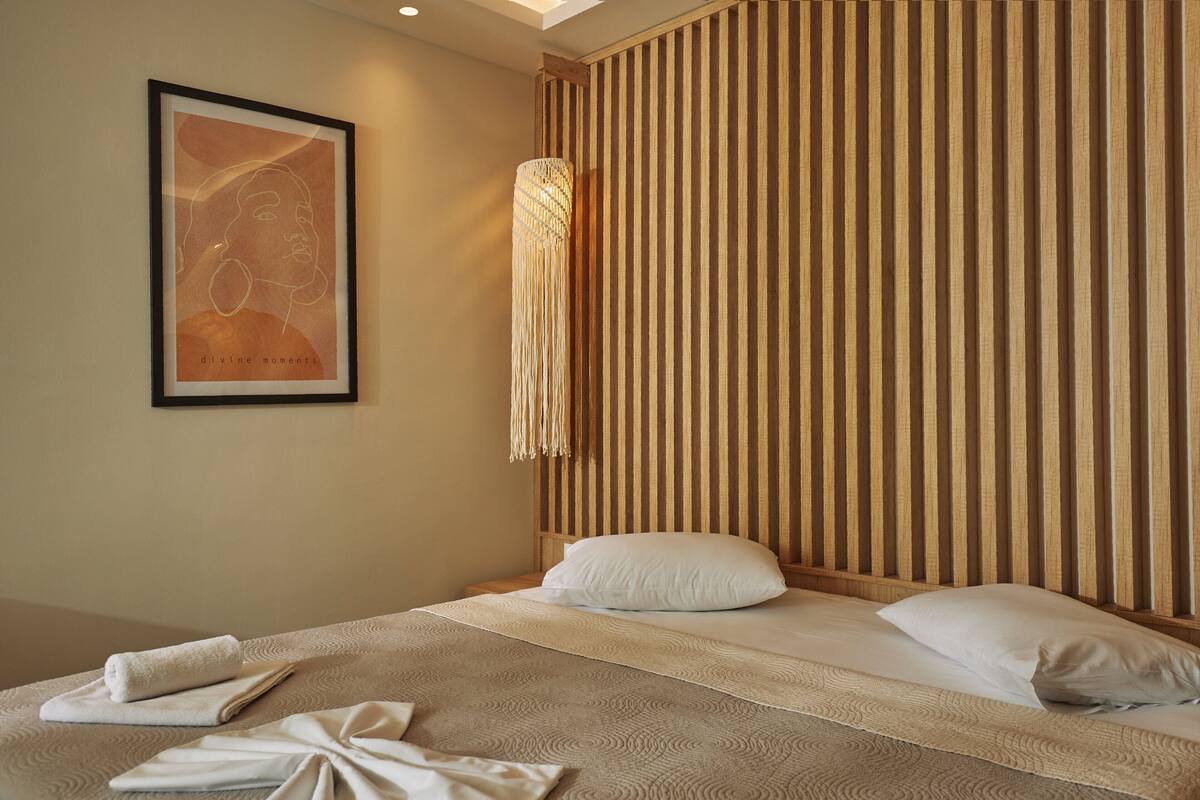 A hotel room with a bed, a framed artwork on the wall, and a textured wall panel.