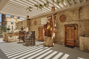 A covered outdoor area with a rustic wooden door, a large barrel, and a hanging bell.
