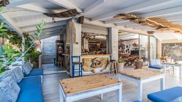 Un’accogliente area salotto esterna con divani blu e tavoli di legno, immersa in elementi naturali e con un’atmosfera rustica al bar.