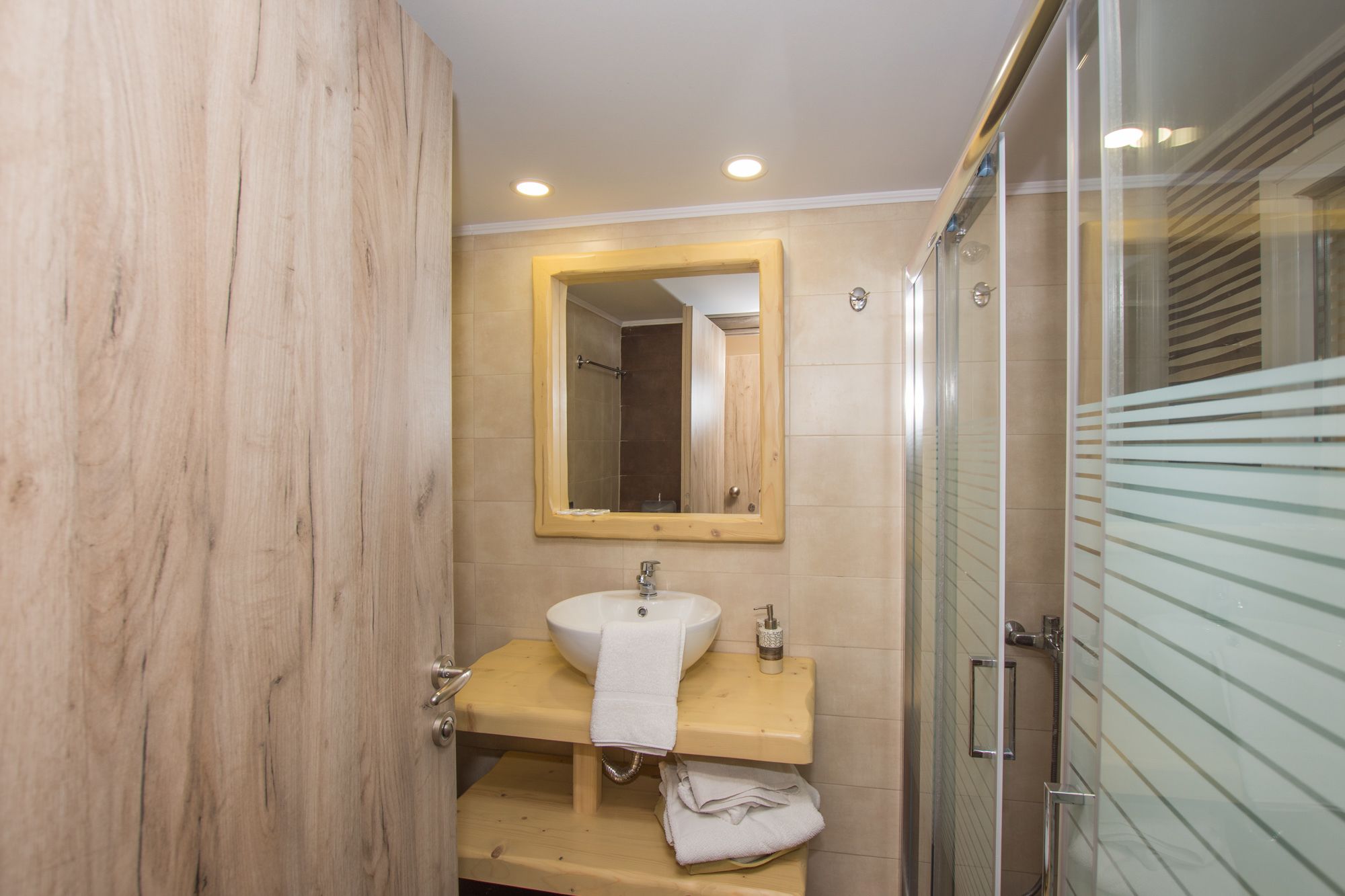 Une salle de bain avec un meuble-lavabo en bois, un lavabo avec une serviette, un miroir et une cabine de douche en verre.