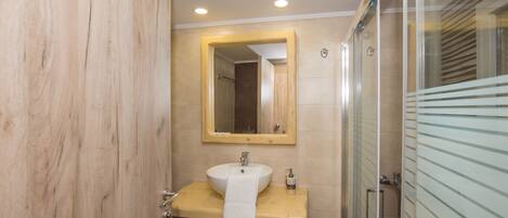 Une salle de bain avec un meuble-lavabo en bois, un lavabo avec une serviette, un miroir et une cabine de douche en verre.
