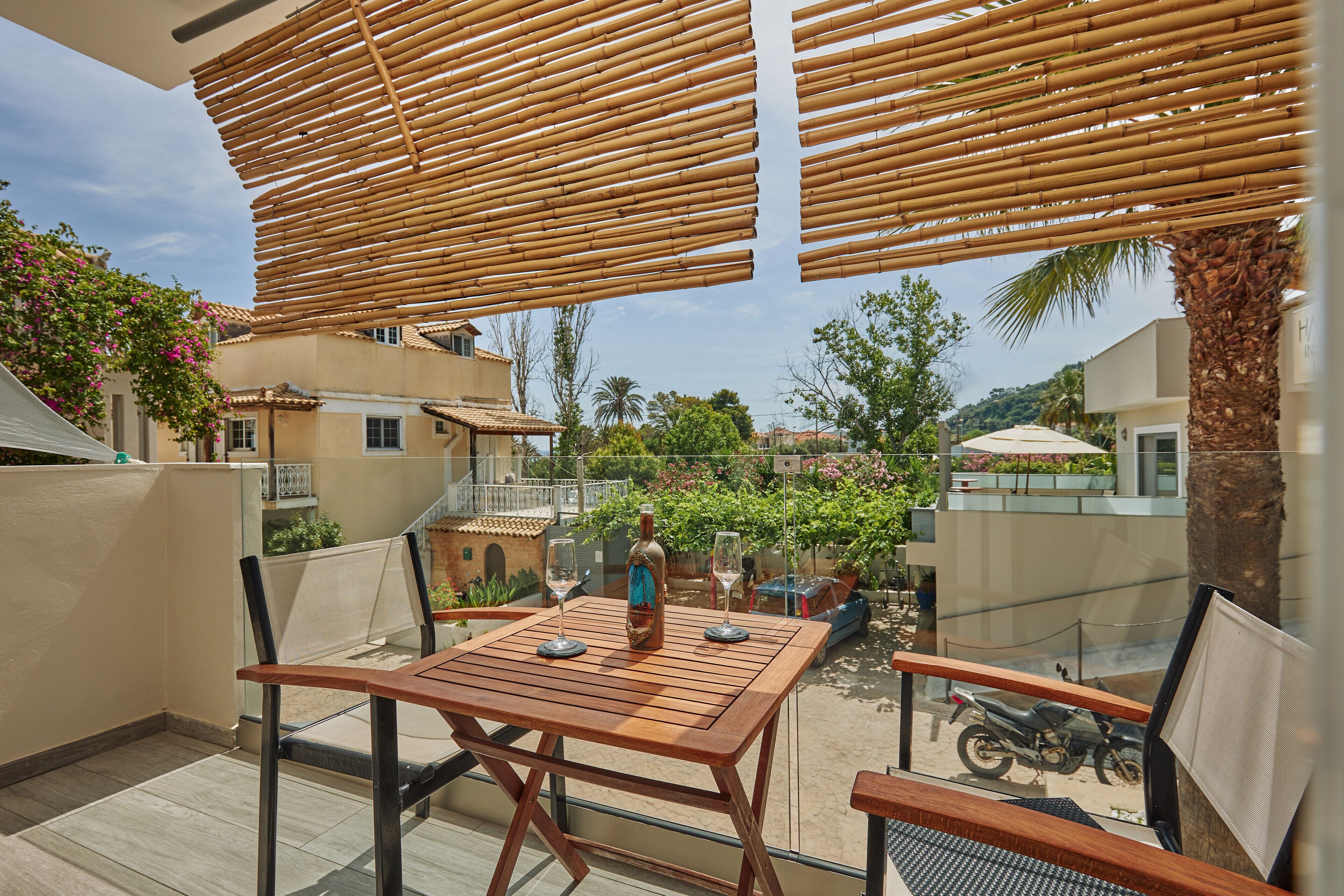 A balcony with a wooden table, two chairs, and a bottle of wine.