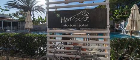 A sign for InioHOS Hotel with a pool and bicycles in the foreground.