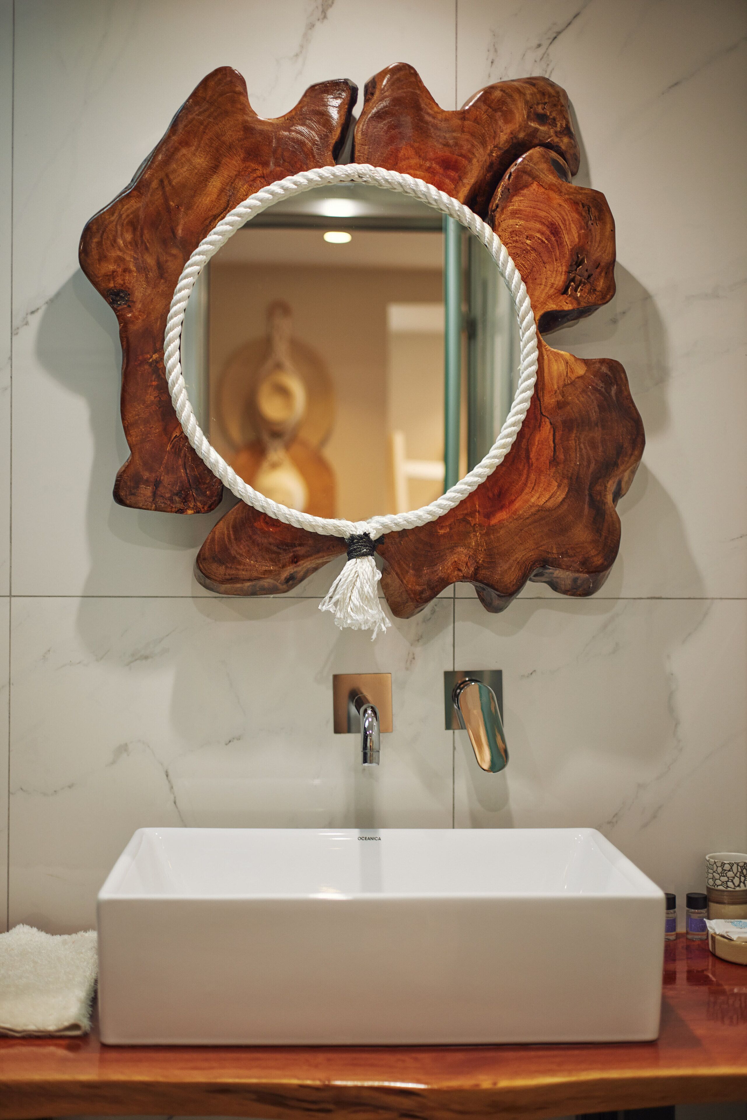 Un baño con lavamanos blanco, un espejo con marco de cuerda y una pared de acento de madera.