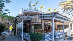A covered outdoor seating area with white benches and a central wicker basket.