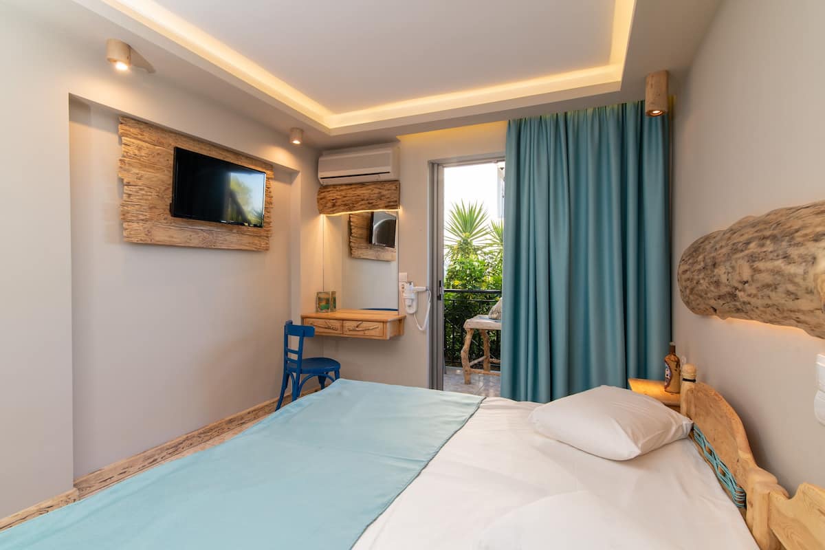 A bedroom with a bed, a desk, a TV mounted on a wooden wall, and a view of the outdoors.