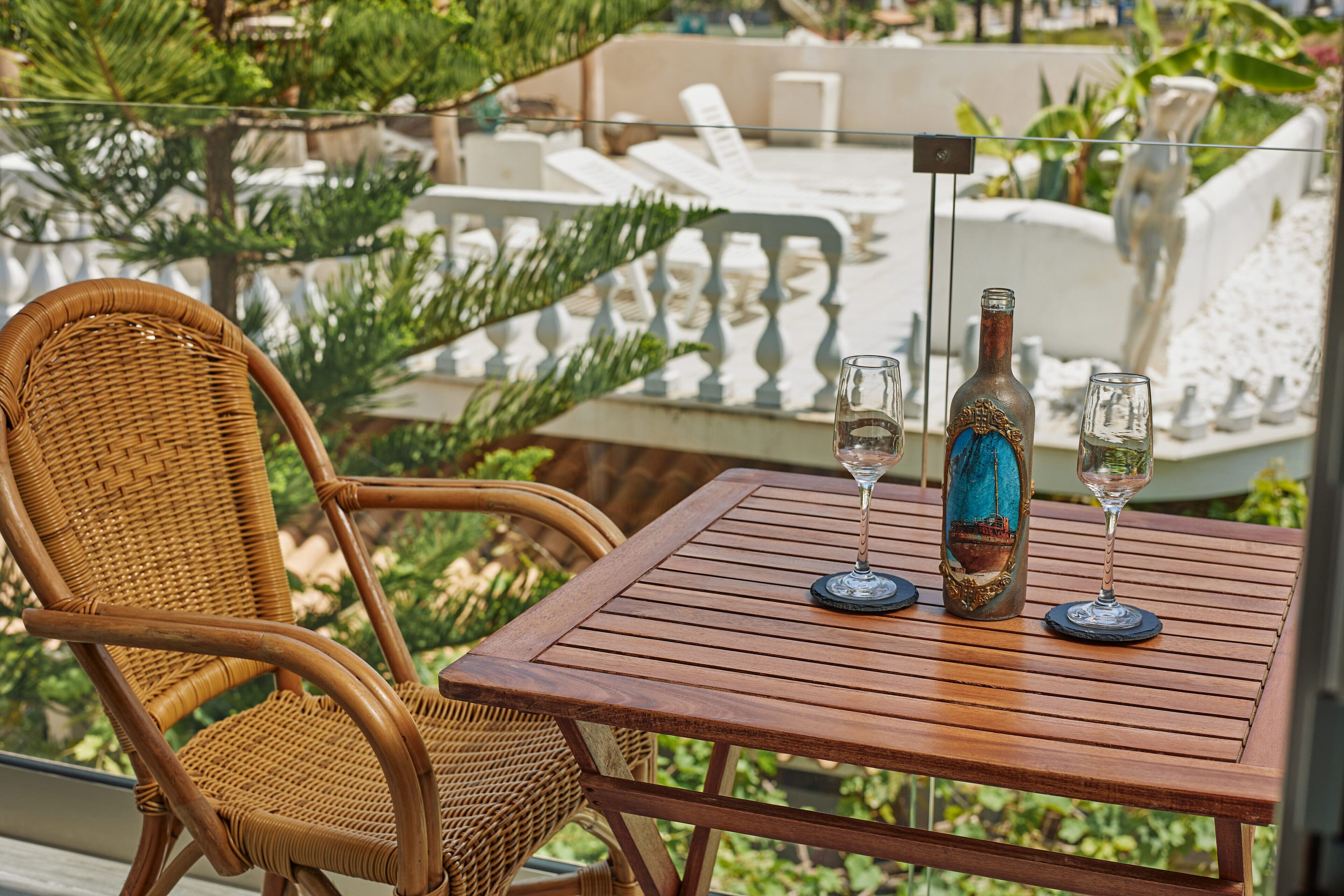 A wicker chair and a wooden table with two wine glasses and a bottle.