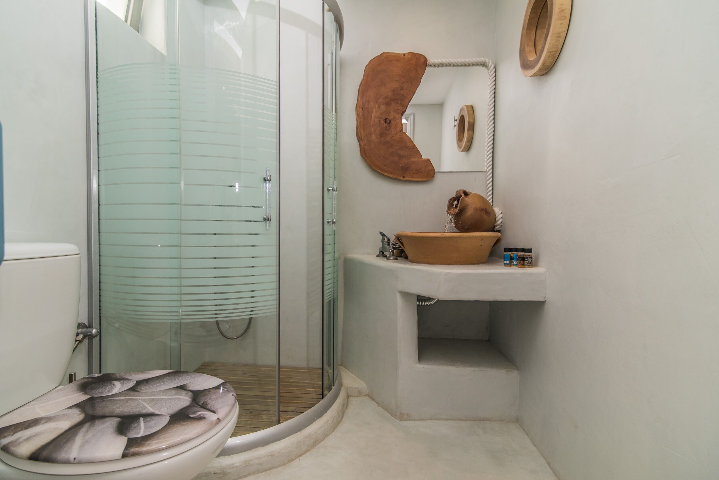 Un baño con cabina de ducha de vidrio, inodoro con un diseño de tapa original, lavabo con cuenco de madera y espejo con marco de madera.