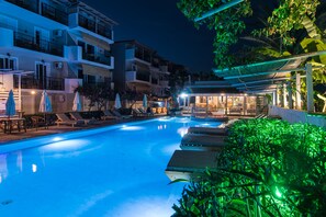 A swimming pool with lounge chairs and umbrellas, surrounded by multi-story buildings with balconies and outdoor seating areas.