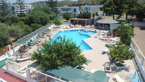 Piscina cercada por espreguiçadeiras e guarda-sóis, com edifícios ao fundo.