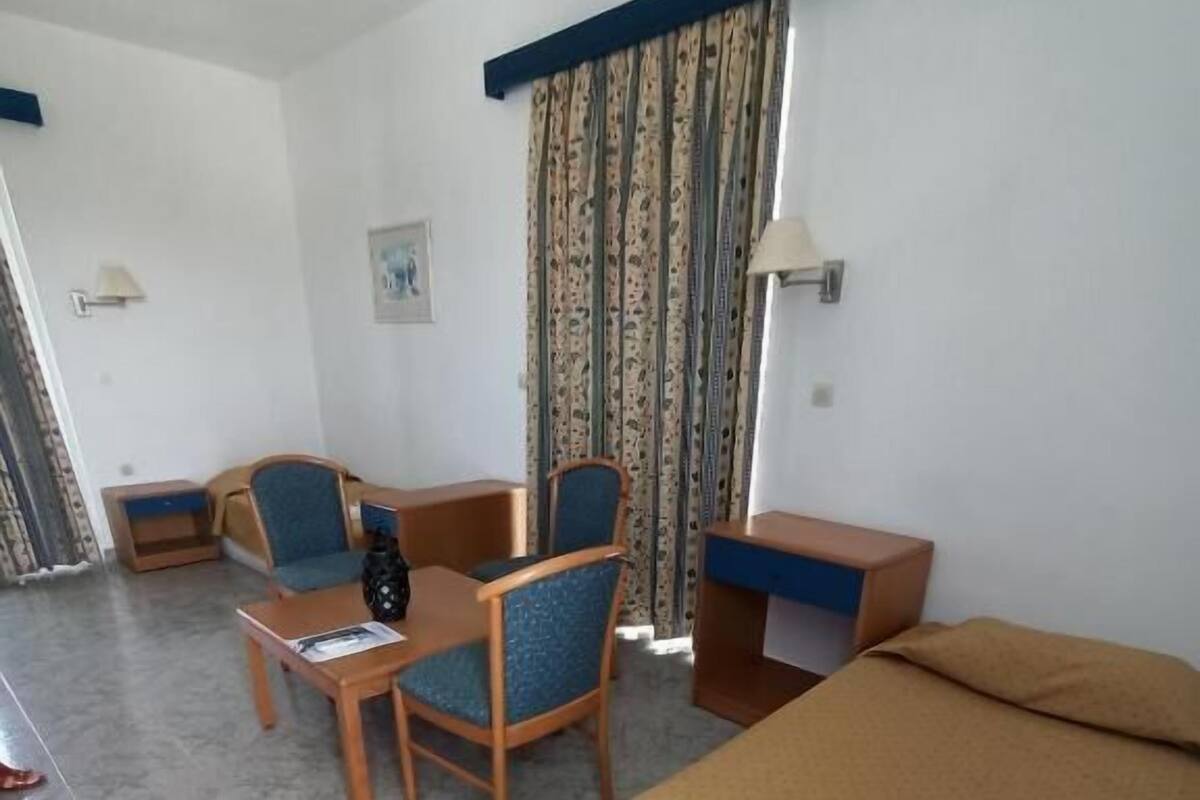 Hotellihuone, jossa on sänky, työpöytä, kaksi tuolia, pieni pöytä ja verhot.