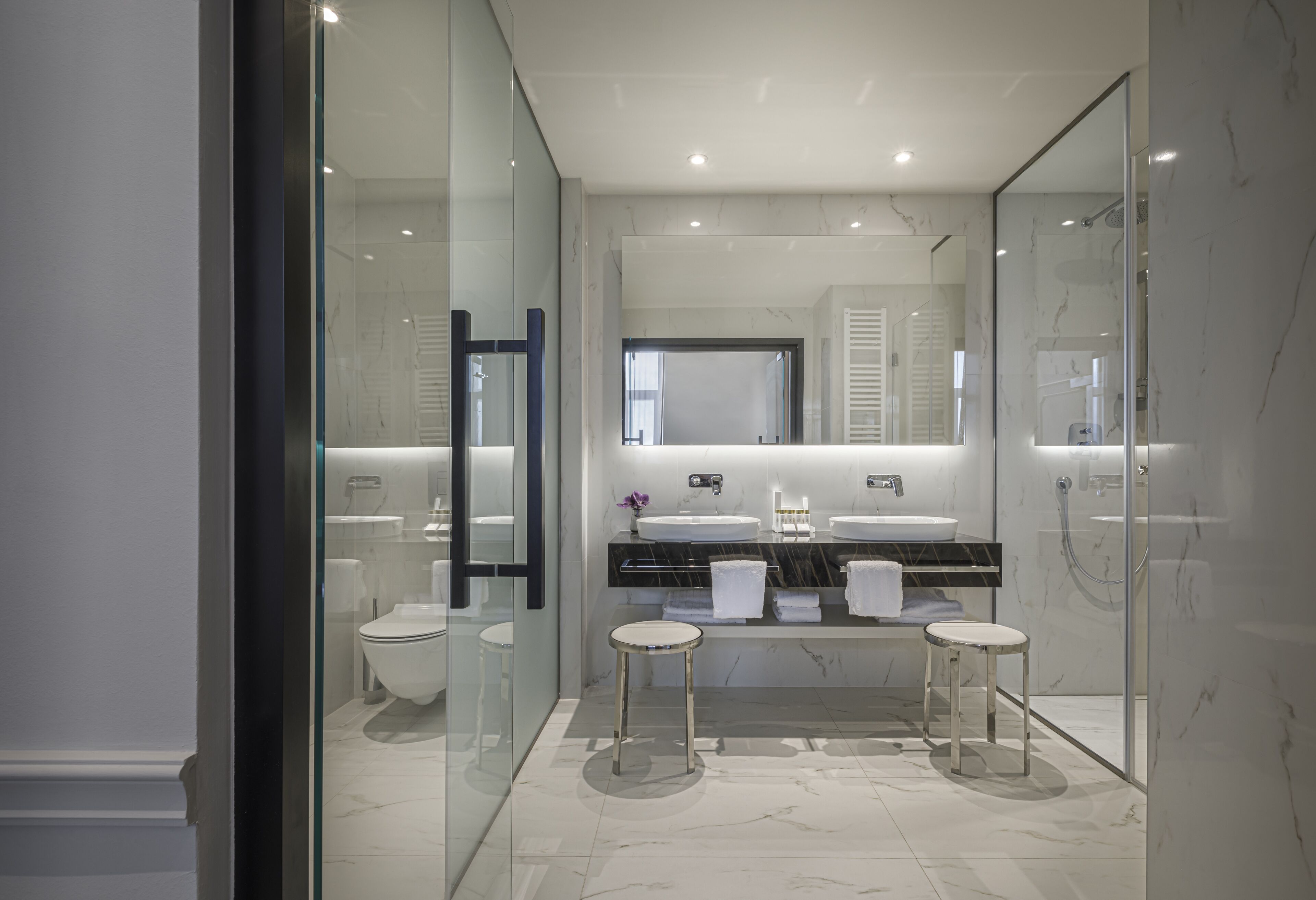A modern bathroom with two sinks, a glass-enclosed shower, and a large mirror.