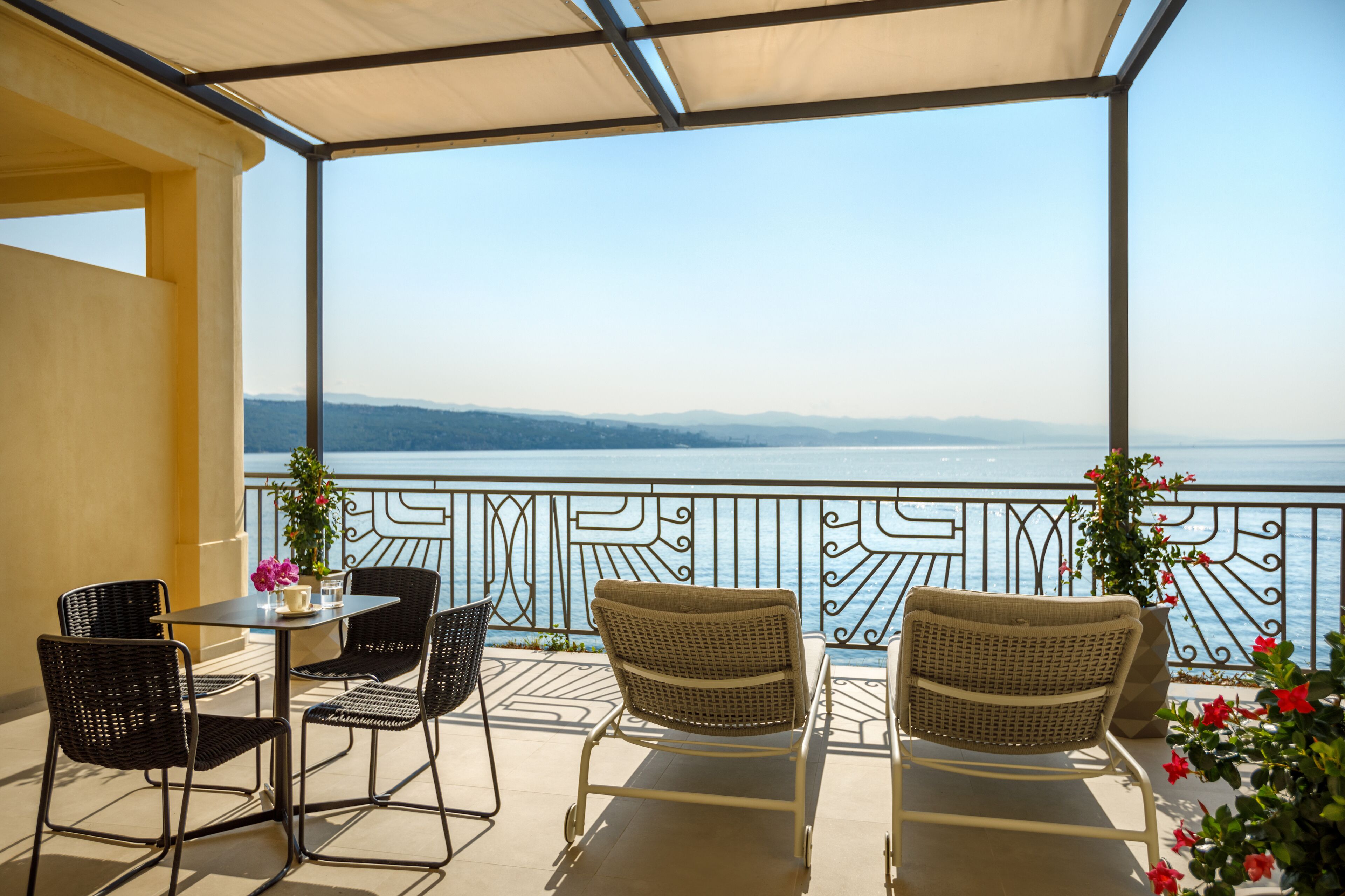 Een balkon met rieten stoelen en een tafel, met uitzicht op een waterpartij en verre bergen.