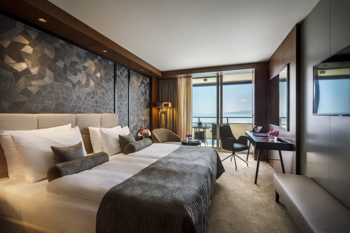 A hotel room with a large bed, a desk, a chair, and a view of the sea.